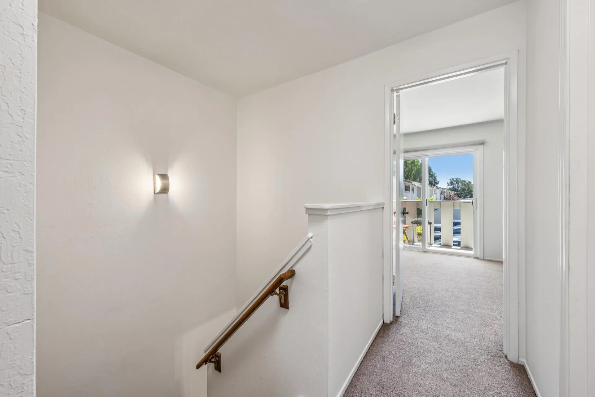 Upstairs landing and hallway with wood handrail, sconce, and natural light from bedroom