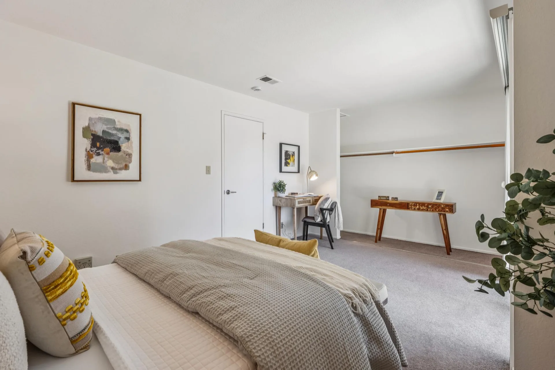 Bedroom with queen bed, writing desk, task lamp, and chair with throw blanket