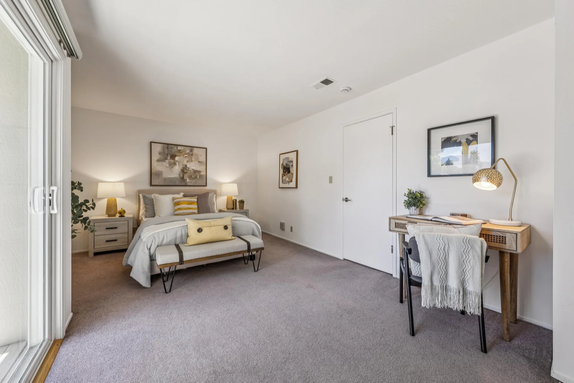 Bedroom suite with sliding glass door, writing desk area, and long bench at foot of bed