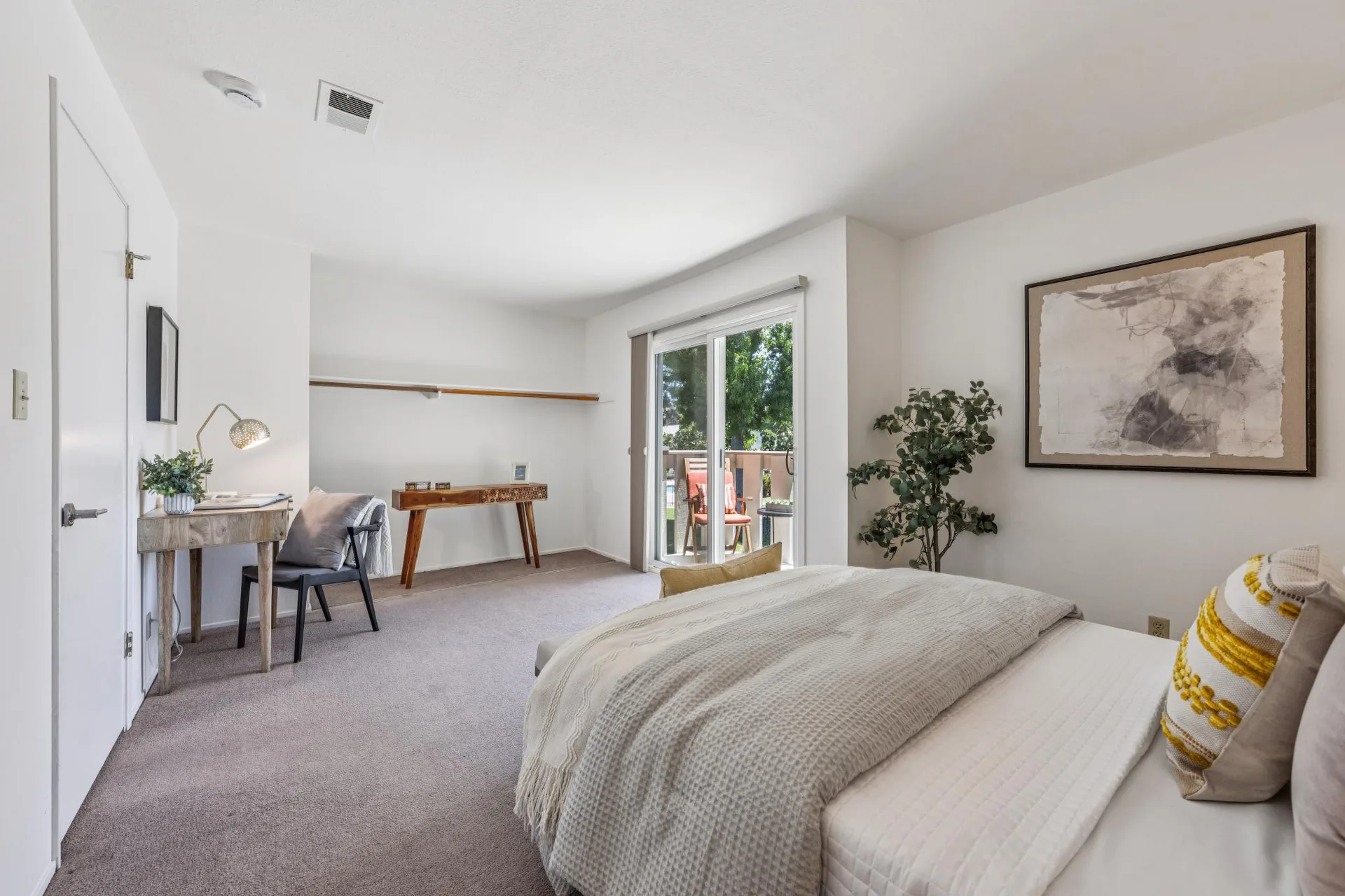 Bedroom with bed, desk with lamp, chair, and large wall art
