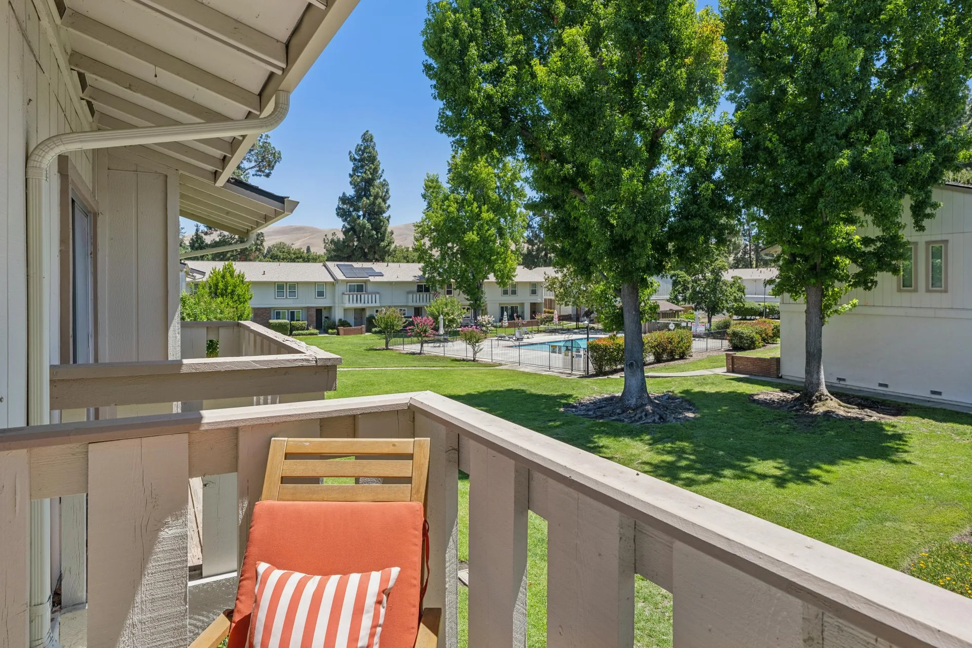 Elevated balcony view overlooking community grounds, swimming pool, and mature trees