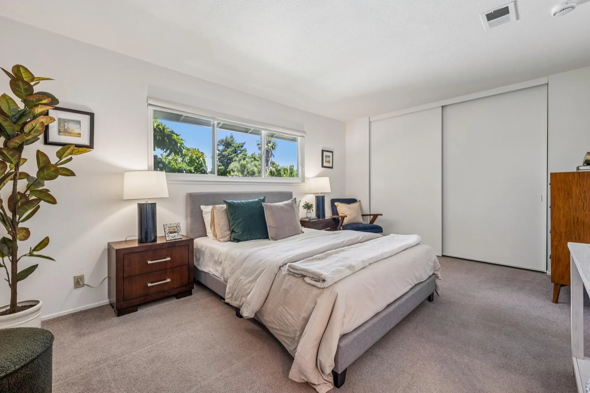 Bedroom with upholstered bed frame, armchair, wood dresser, and large plant