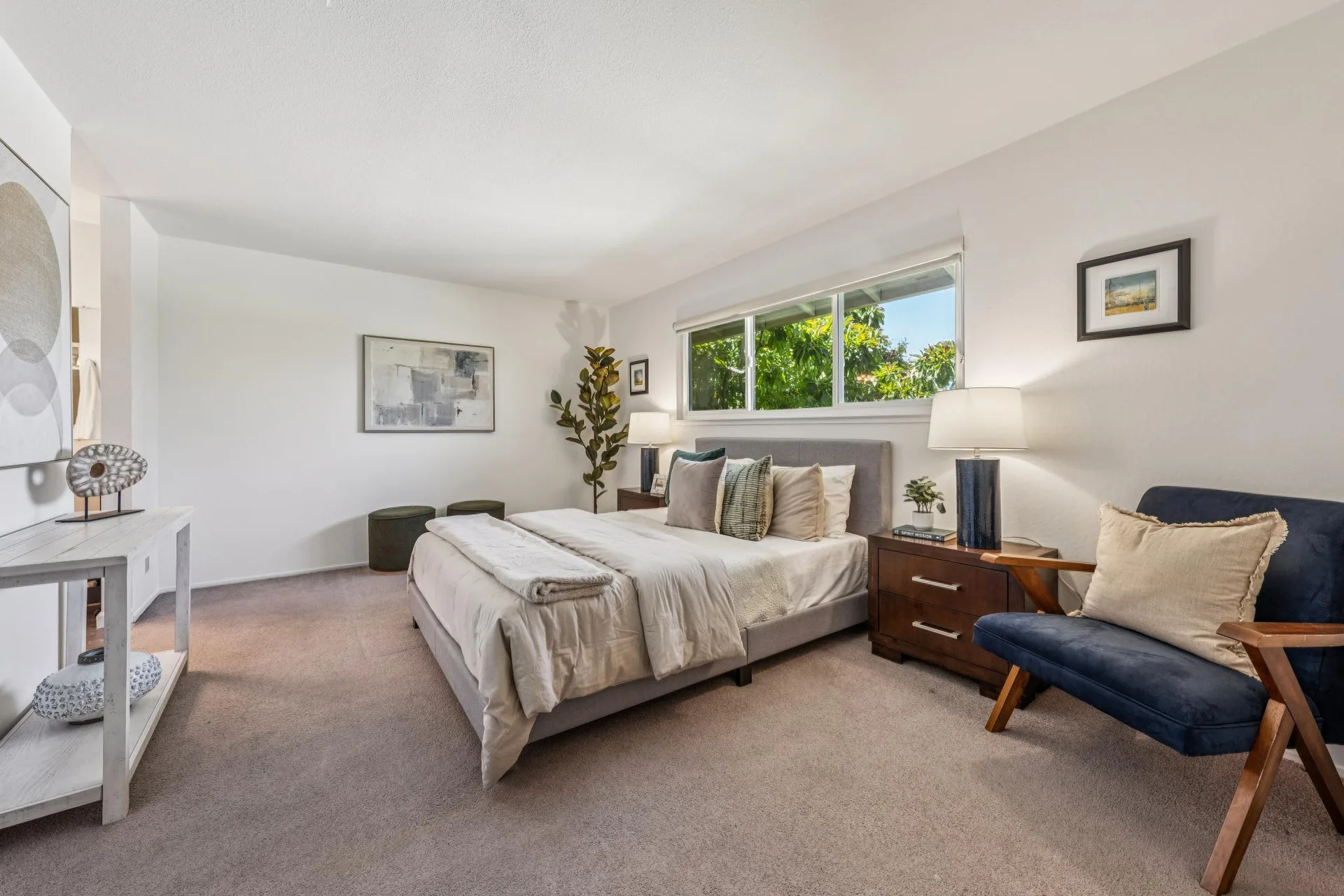 Primary bedroom with tan bedspread, teal accent pillow, blue side chair, and blue lamp bases