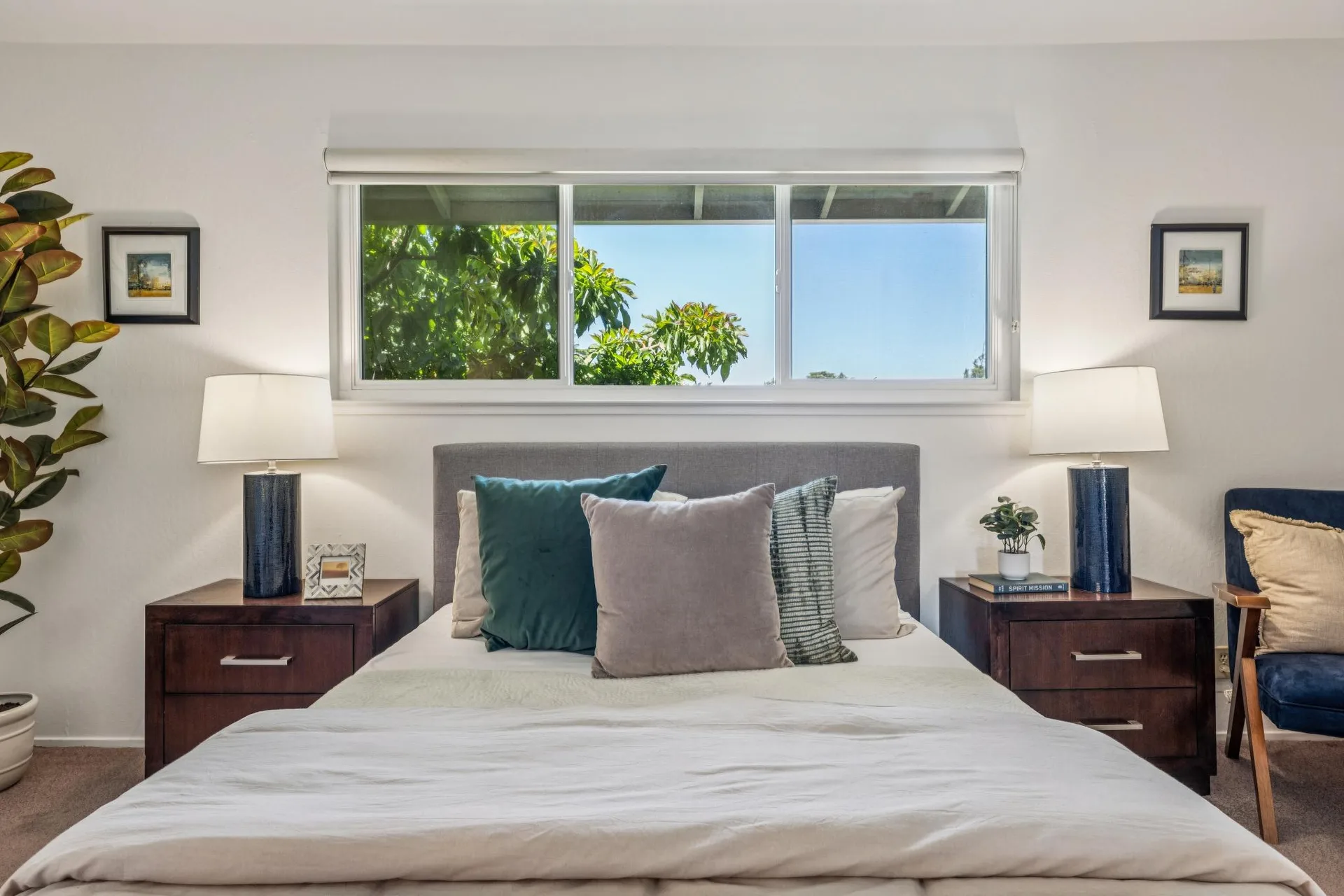 Primary bedroom wide view with tan bedding, blue side chair, dark wood nightstands, and blue table lamps