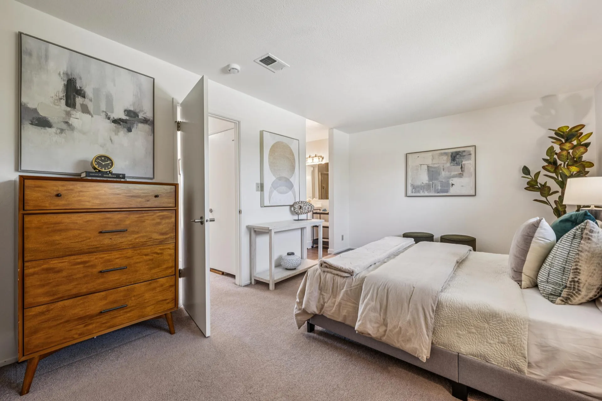 Bedroom interior from foot of bed showing wooden dresser, console table, and two stools