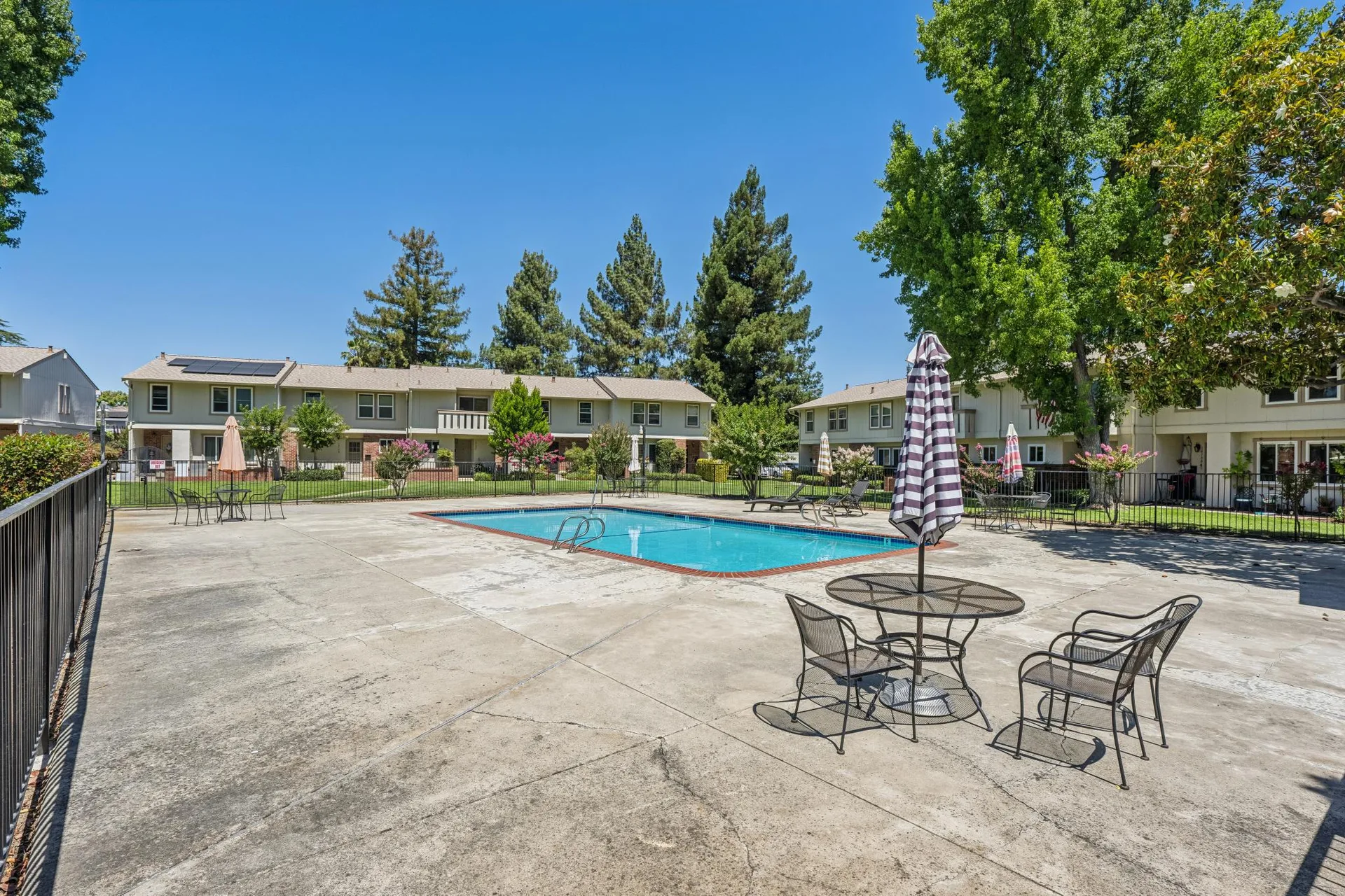 Wide-angle shot of communal swimming pool deck with patio furniture and fencing