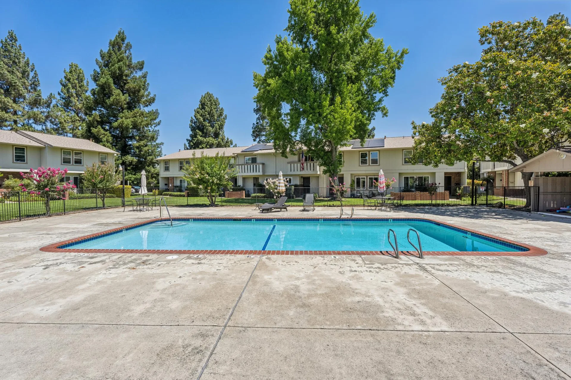 Community swimming pool with concrete deck, brick coping, and lounge chairs