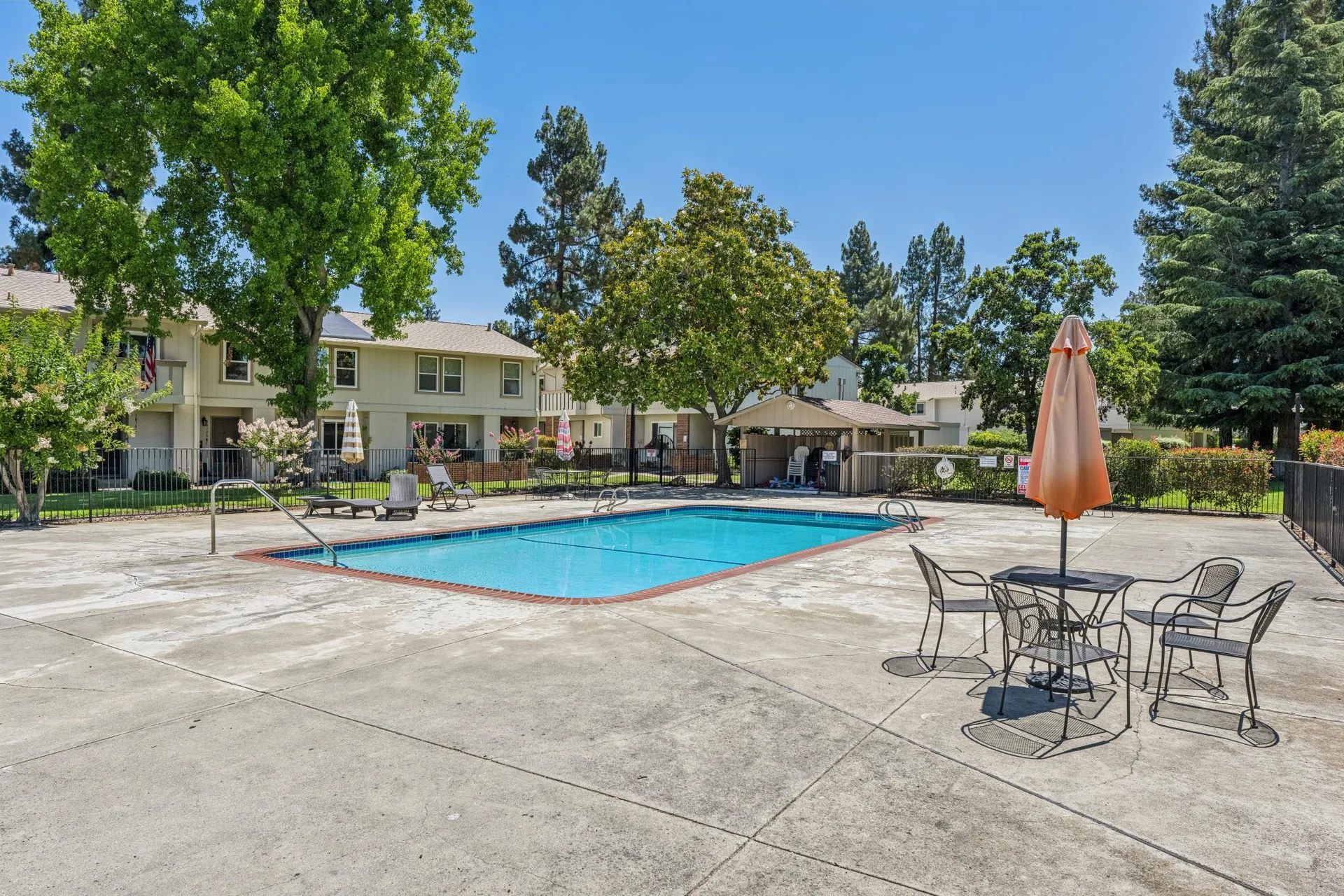 Community pool area in Oak Glen with mature trees, patio umbrella, and bistro set