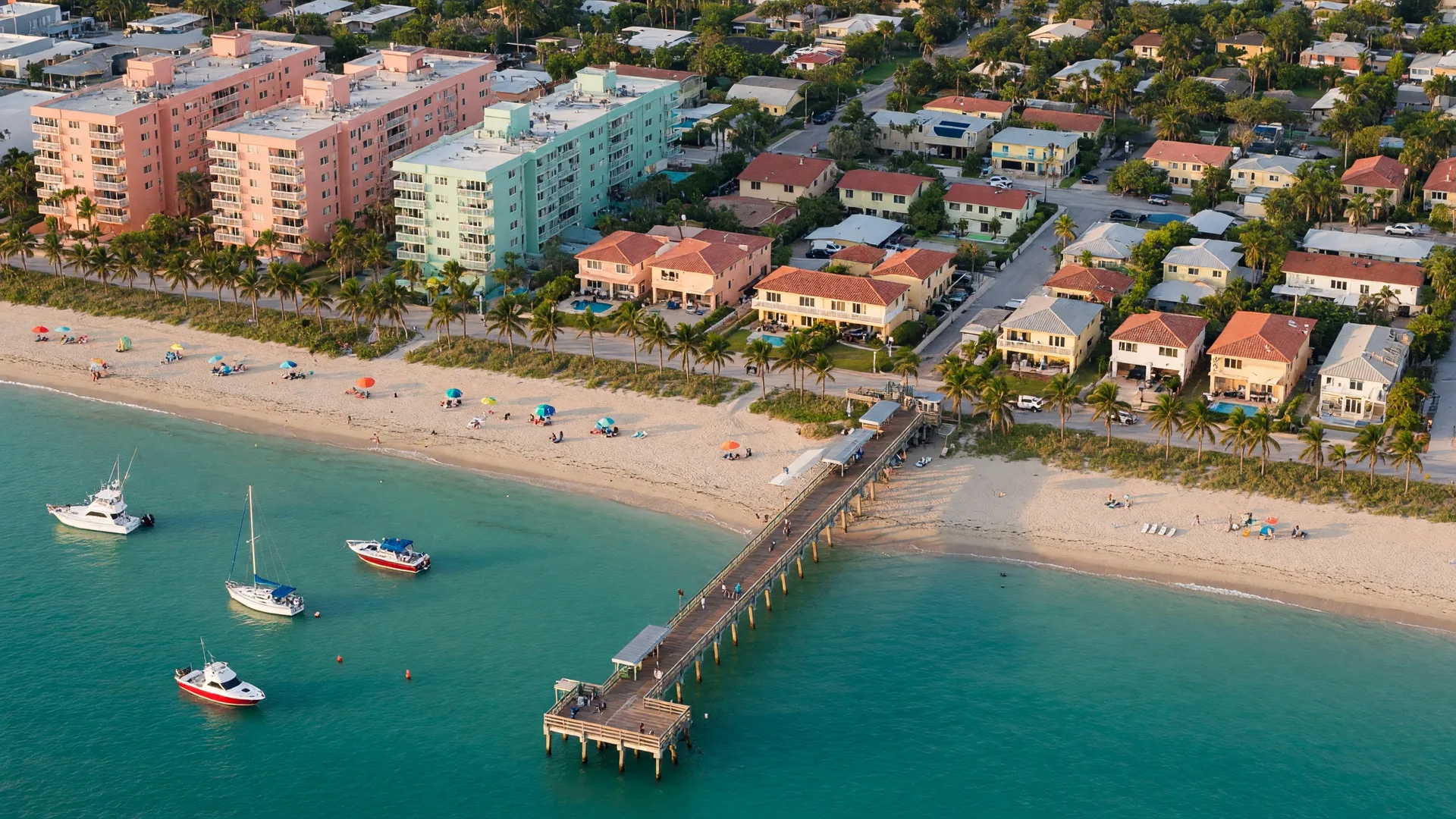 Aerial view of Pompano Beach shoreline with the pier extending over turquoise Atlantic waters, showing condos and homes near the beach