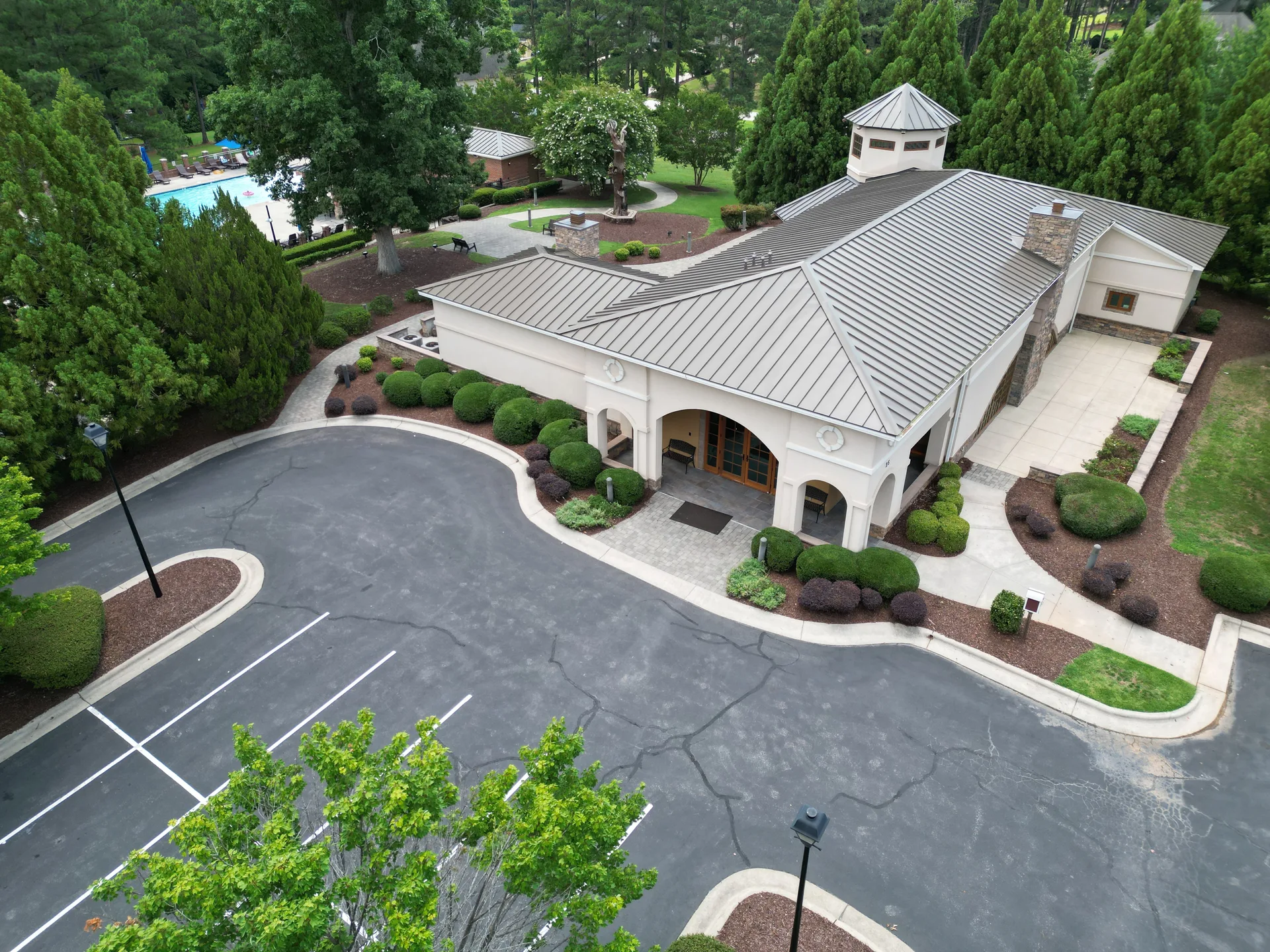 Aerial view of the Portofino community clubhouse with light stucco exterior, dark metal roof, arched entrance, and swimming pool