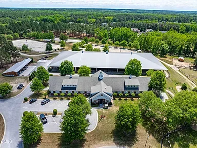 Aerial view of the Portofino equestrian center with farmhouse-style barn and covered arena in a wooded setting