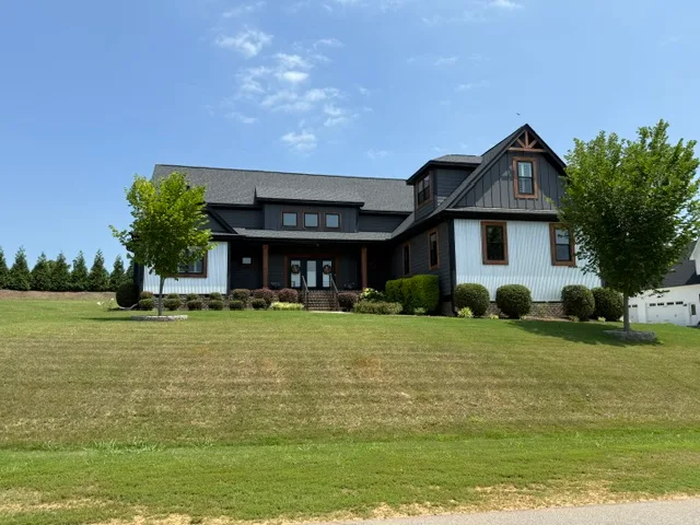 Dark charcoal modern farmhouse on a grassy hill with white board-and-batten accents