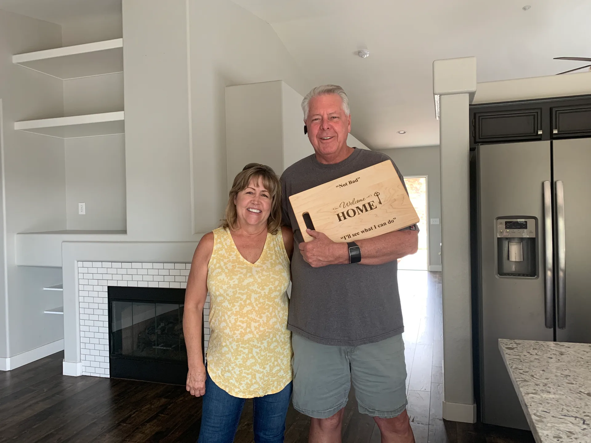 A couple standing together in a modern kitchen holding a wood-engraved welcome home gift