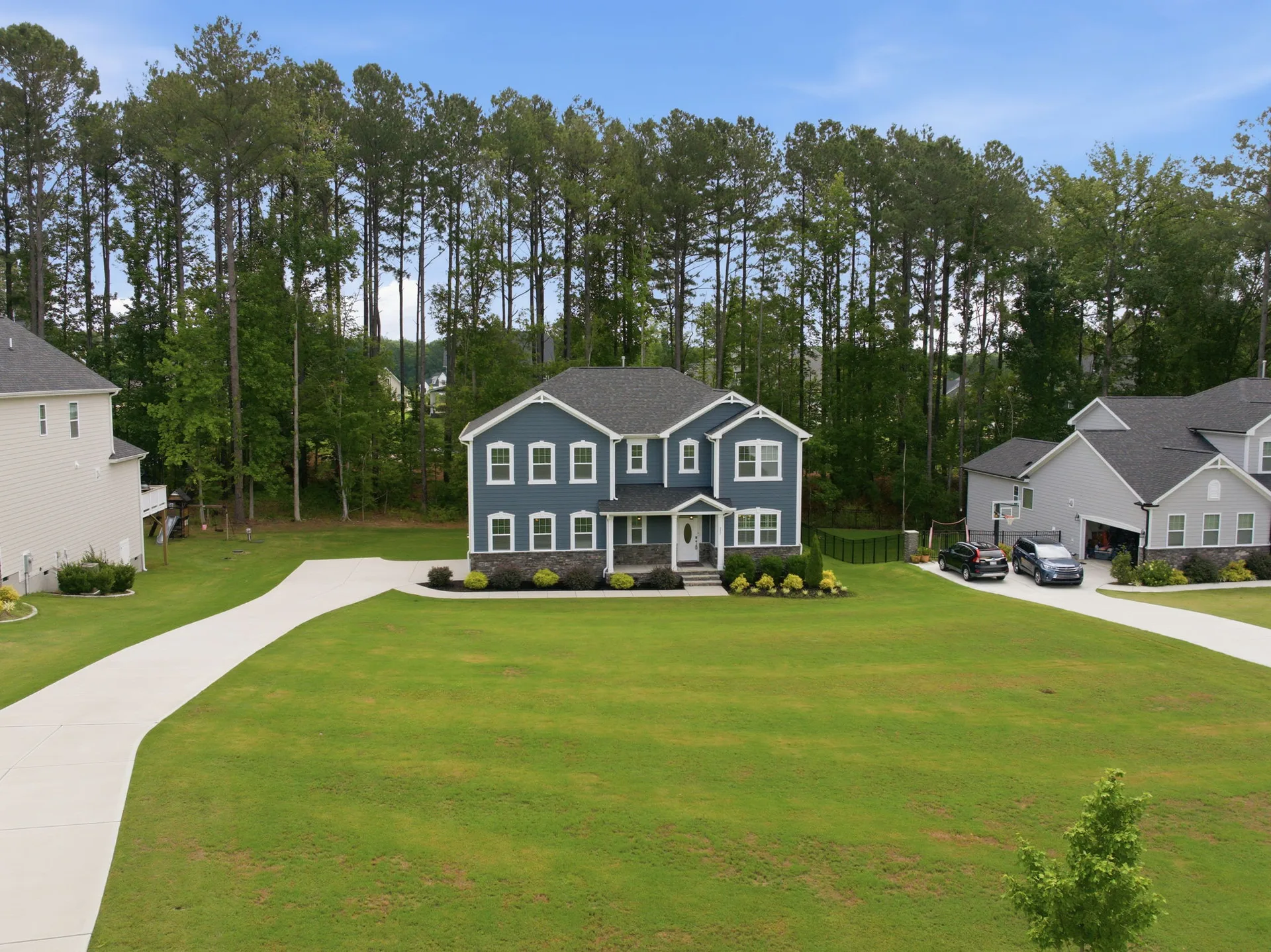 Aerial angled front view of 297 Bonaventure Dr showing the half-acre private lot, wooded surroundings, and home exterior