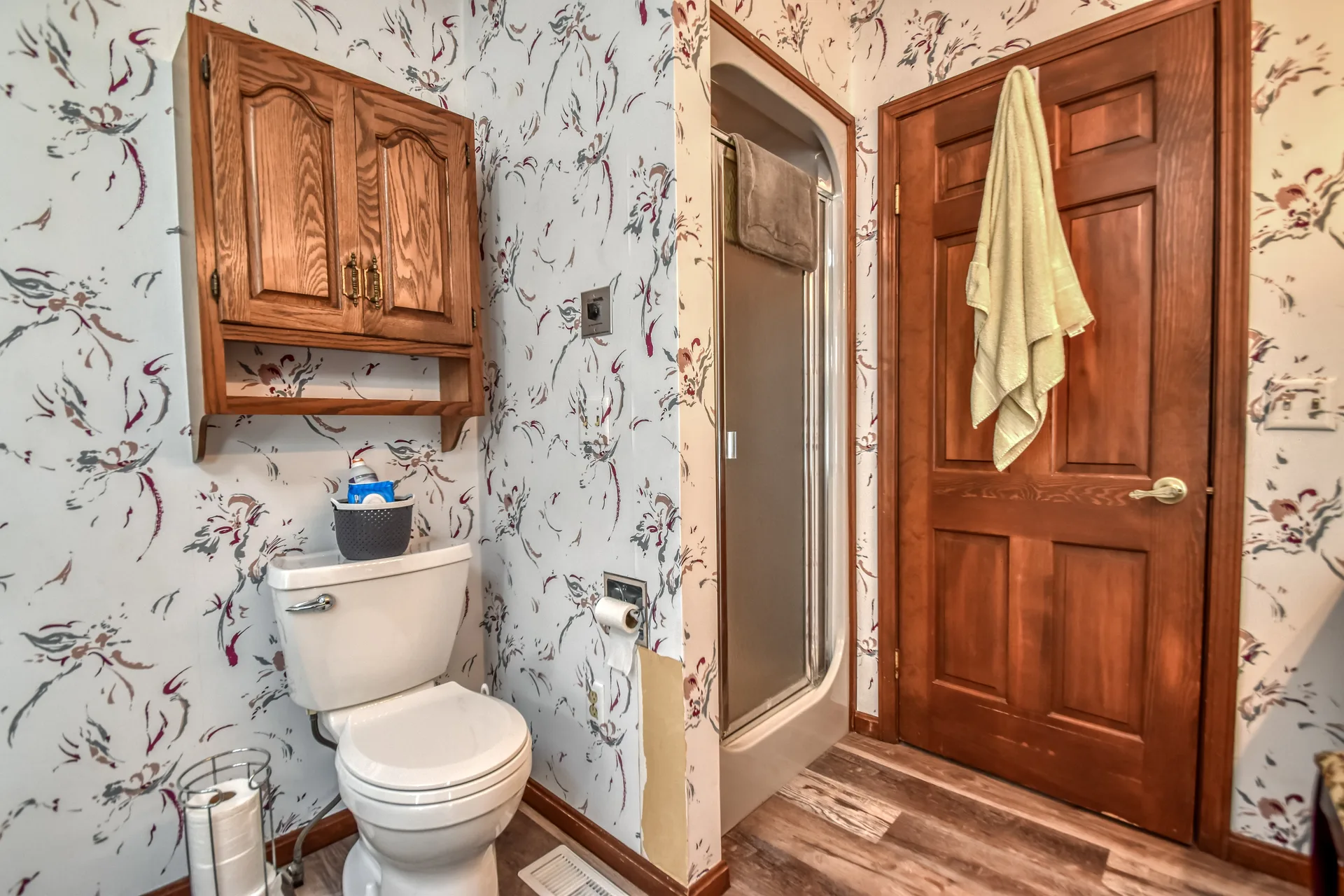 Bathroom with floral wallpaper and wood cabinetry