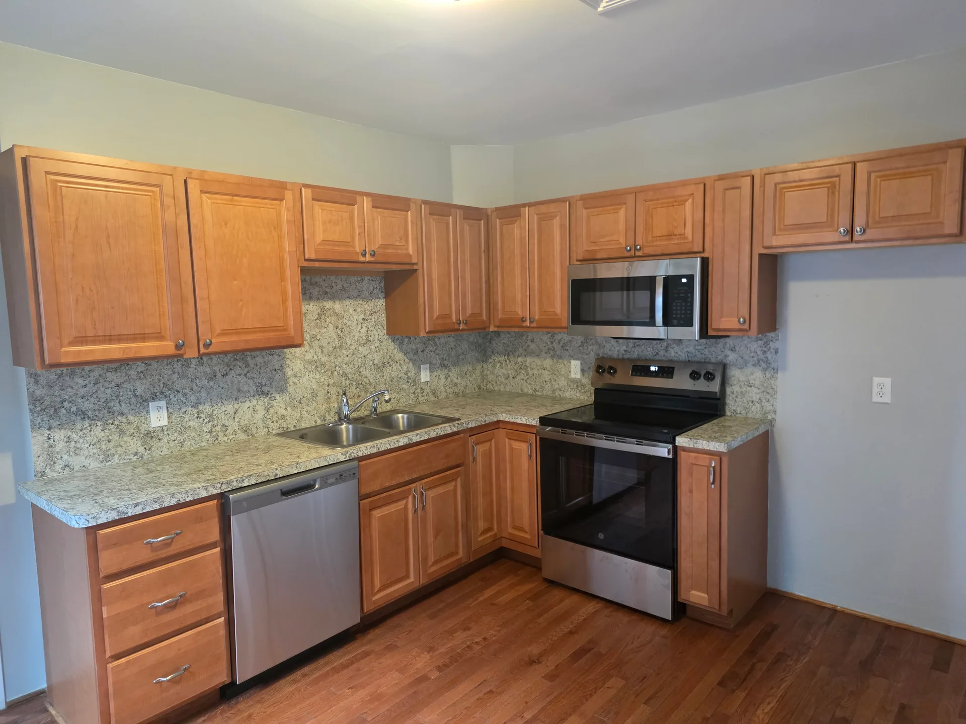 Kitchen with oak cabinetry, granite countertops, stainless steel appliances, and hardwood floors