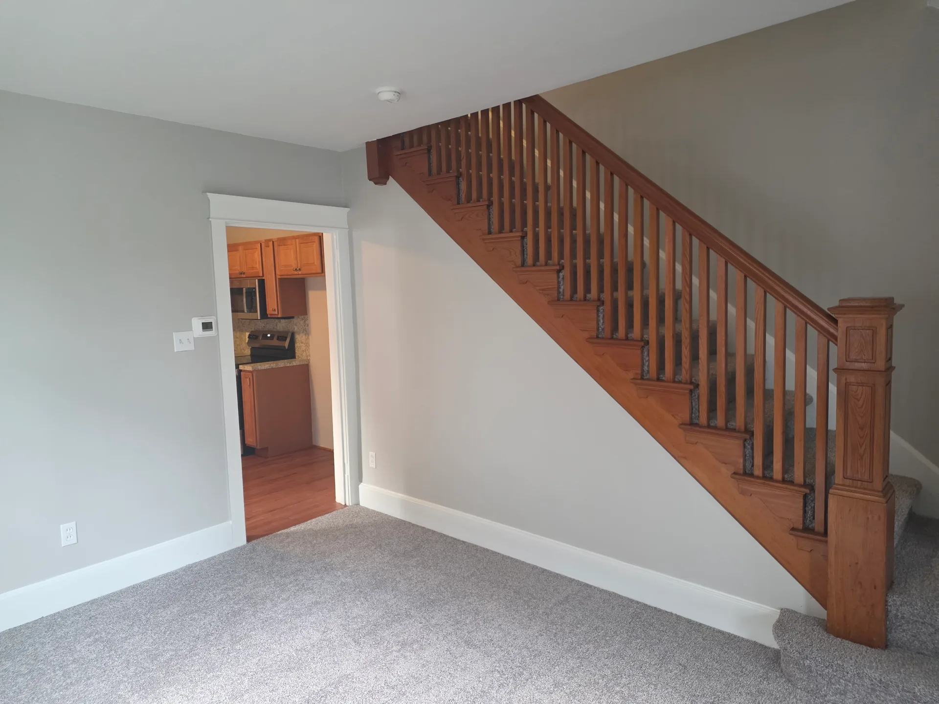 Living area with wooden staircase and new grey carpeting