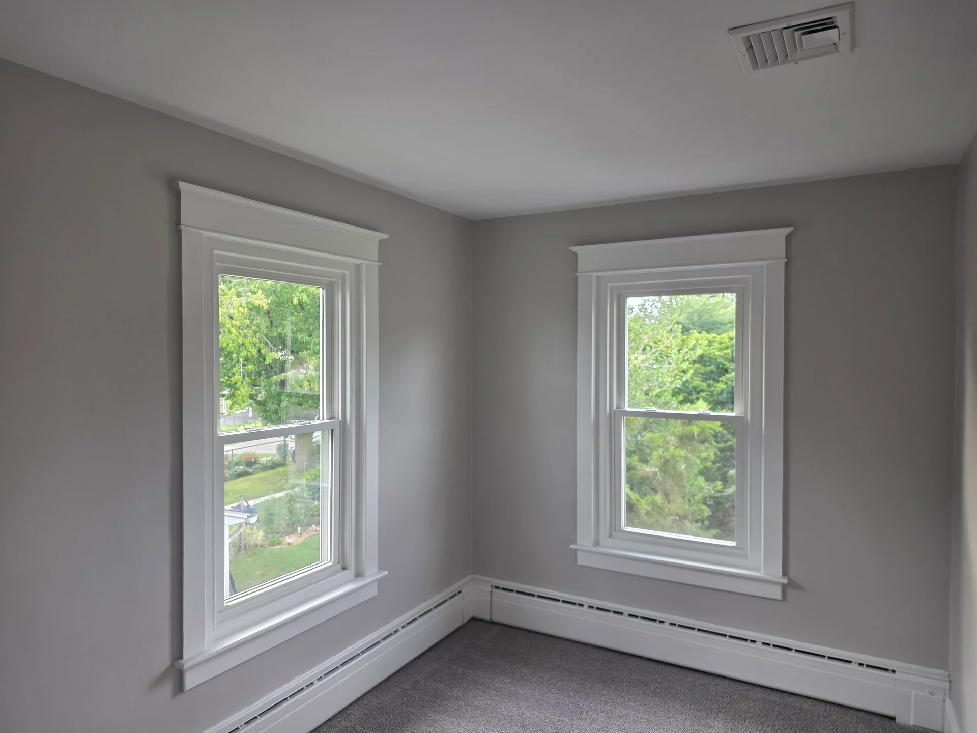 Bedroom corner with two windows and new grey carpeting