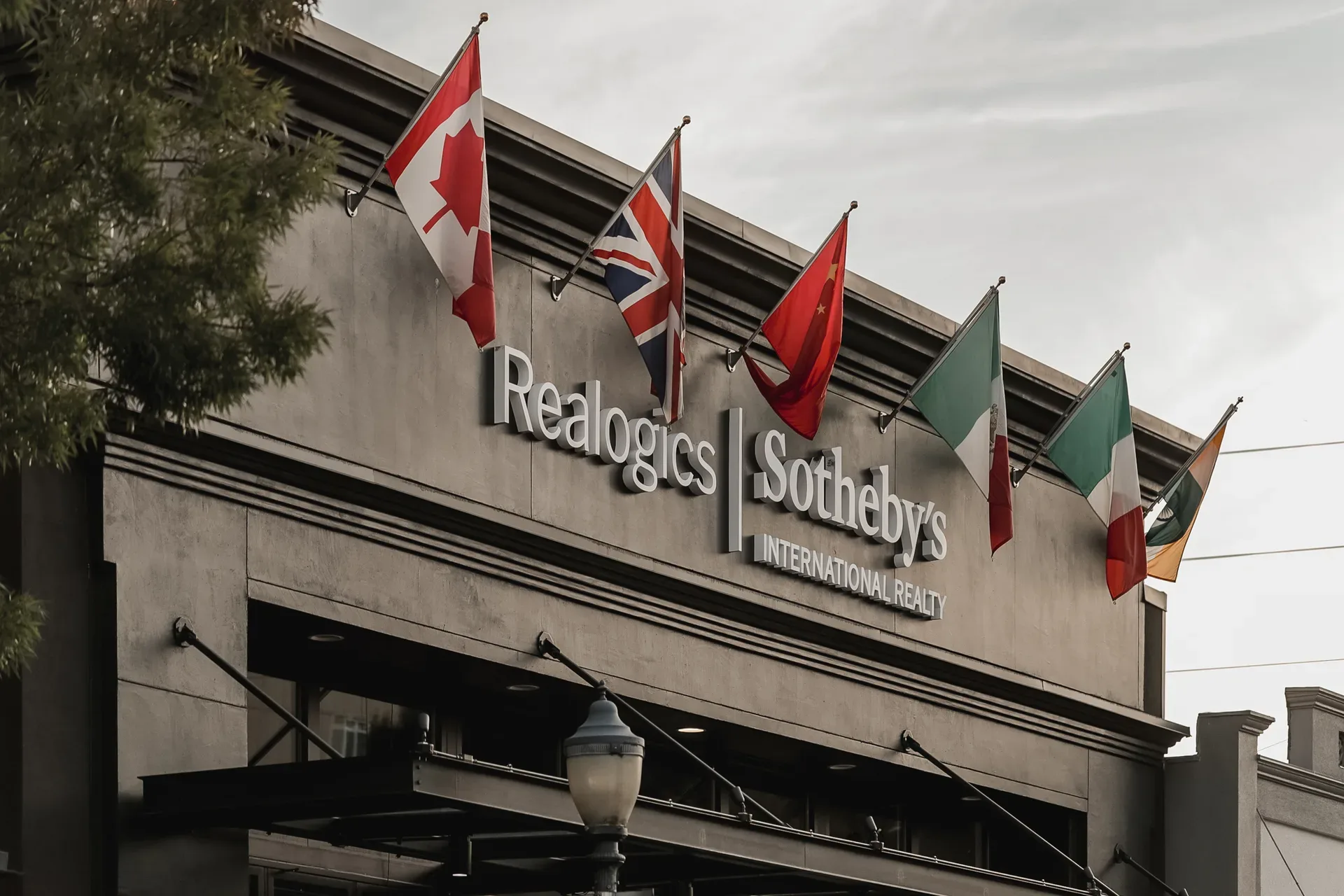 Daytime exterior of the Realogics Sotheby's International Realty office in downtown Bellevue — modern dark facade with white 3D signage and international flags