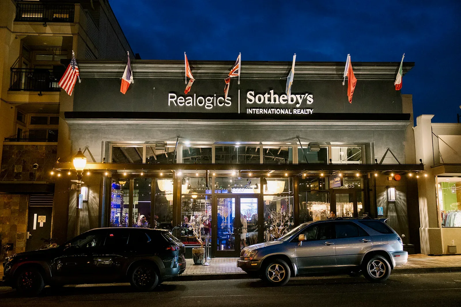 Twilight exterior of the Realogics Sotheby's International Realty office in downtown Bellevue — glowing Edison string lights, illuminated signage, and a warm evening glow