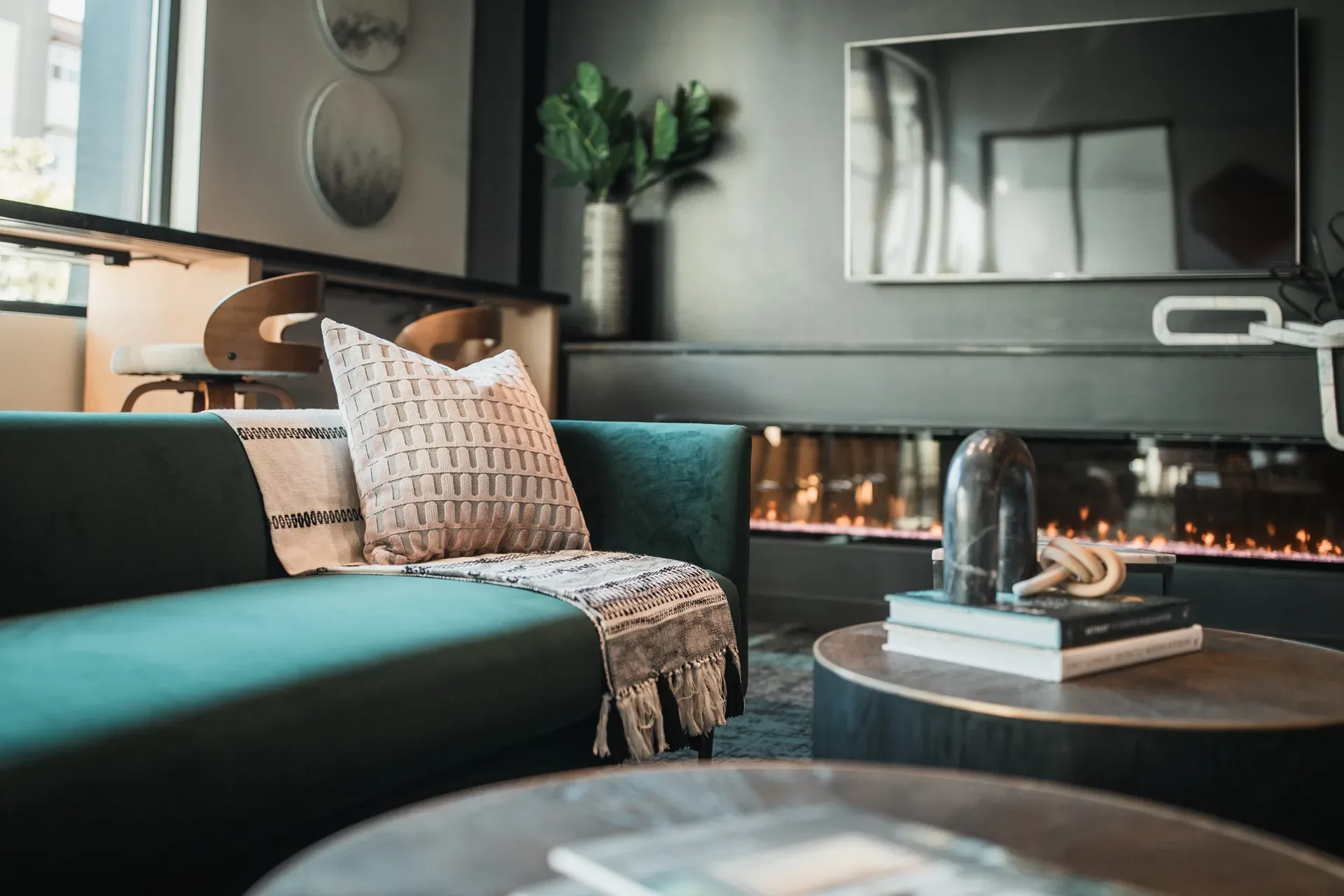 Sophisticated living area at the Sotheby's Bellevue office — deep teal sofa, linear fireplace, coffee table books, and a moody bar area