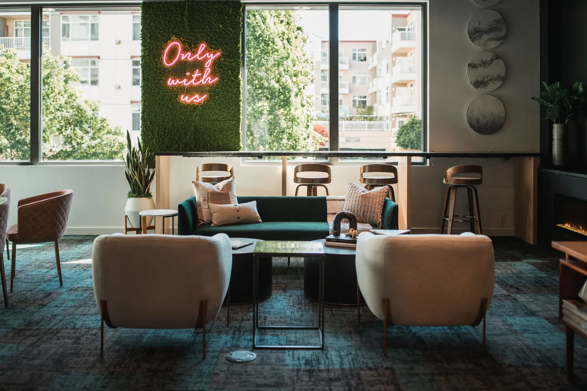 Bright modern lounge at Realogics Sotheby's International Realty Bellevue — plush armchairs, emerald green sofa, neon sign, floor-to-ceiling windows with natural light
