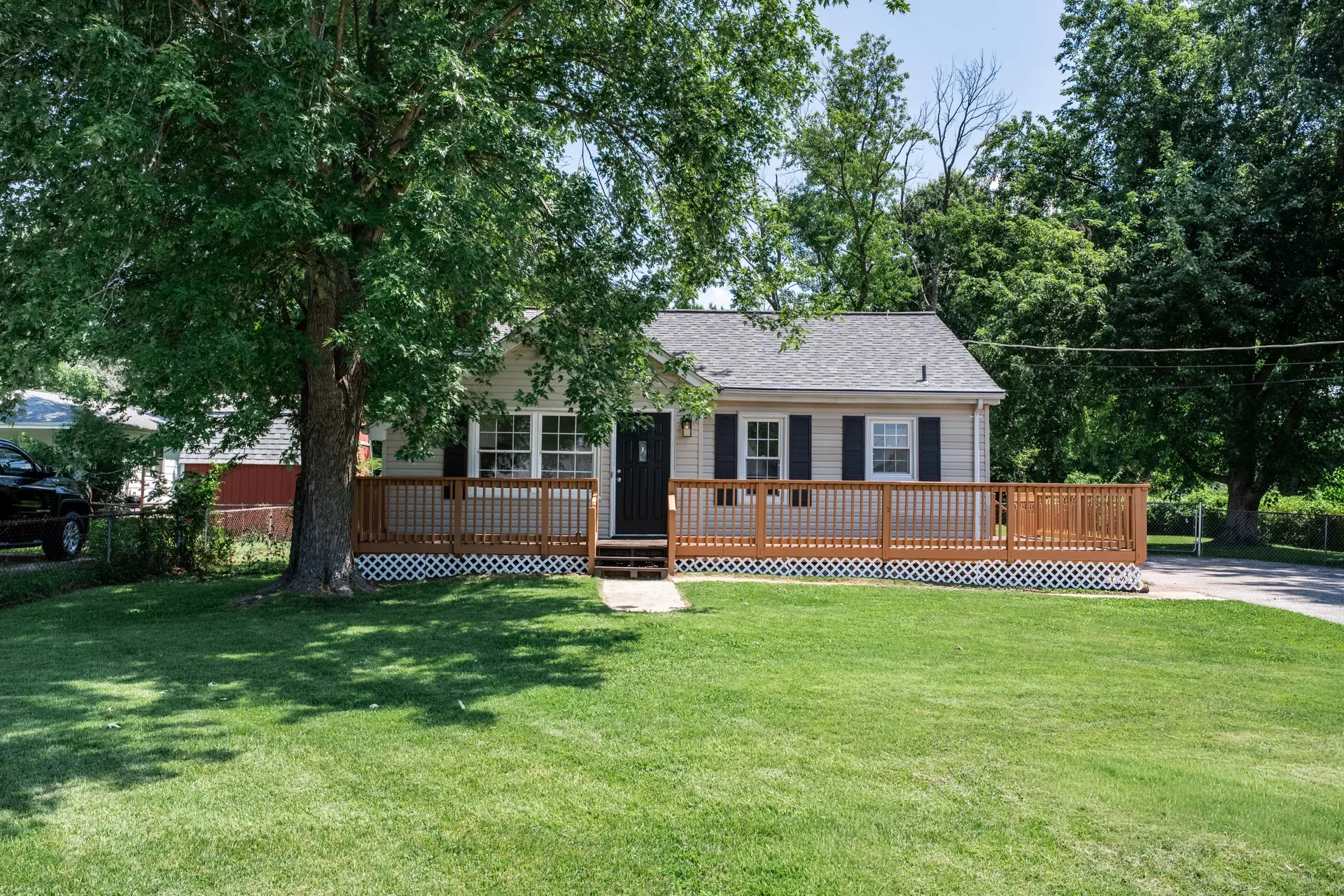Front exterior angle of the ranch-style home showing beige siding, black shutters, front door, and deck
