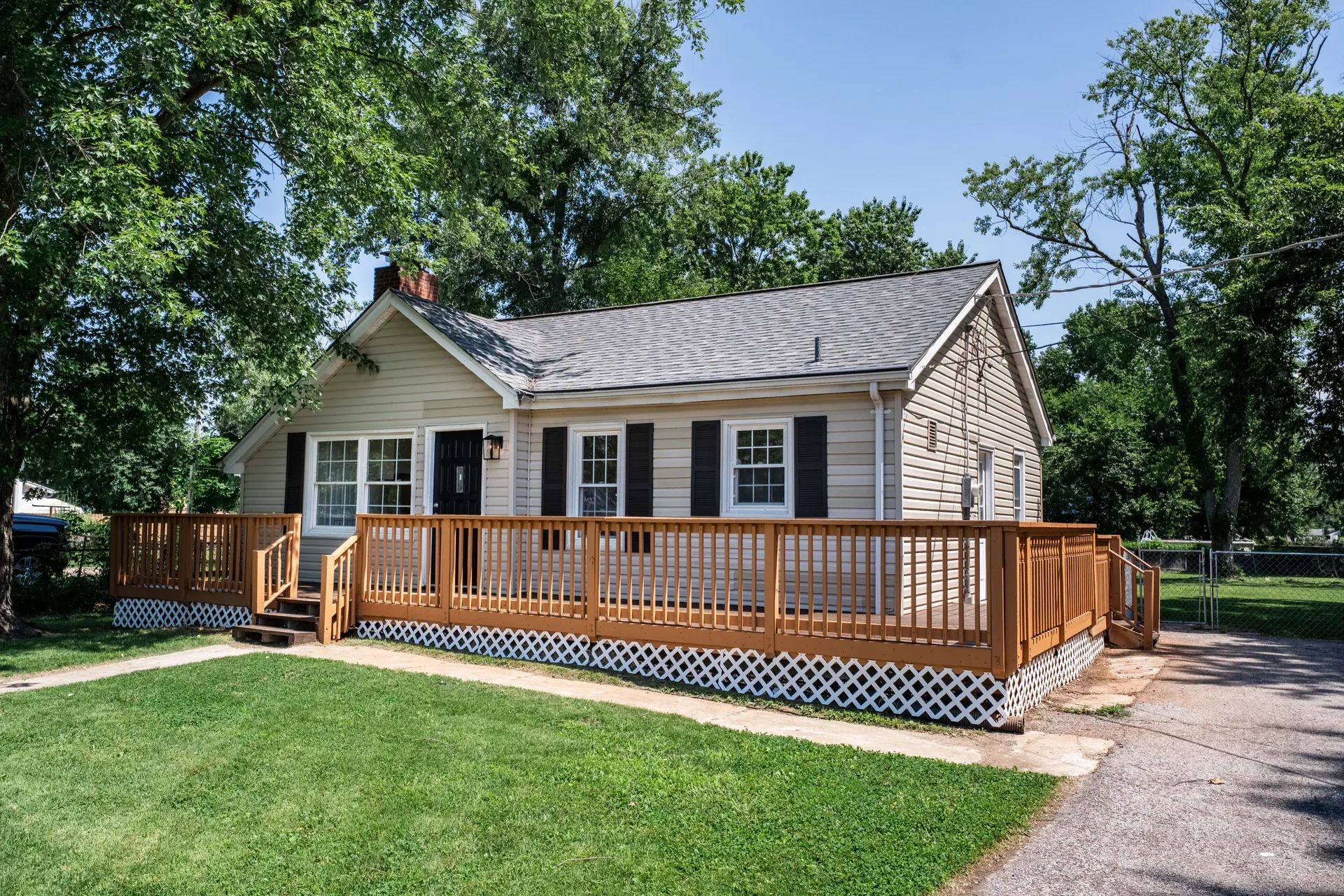 Front side view of the ranch home with vinyl siding, shingled roof, and large wooden front deck with lattice skirting