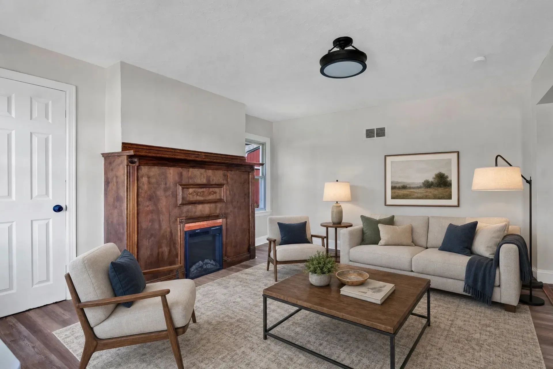 Living room with decorative wood-encased fireplace, LVP flooring, white walls, and staged furnishings