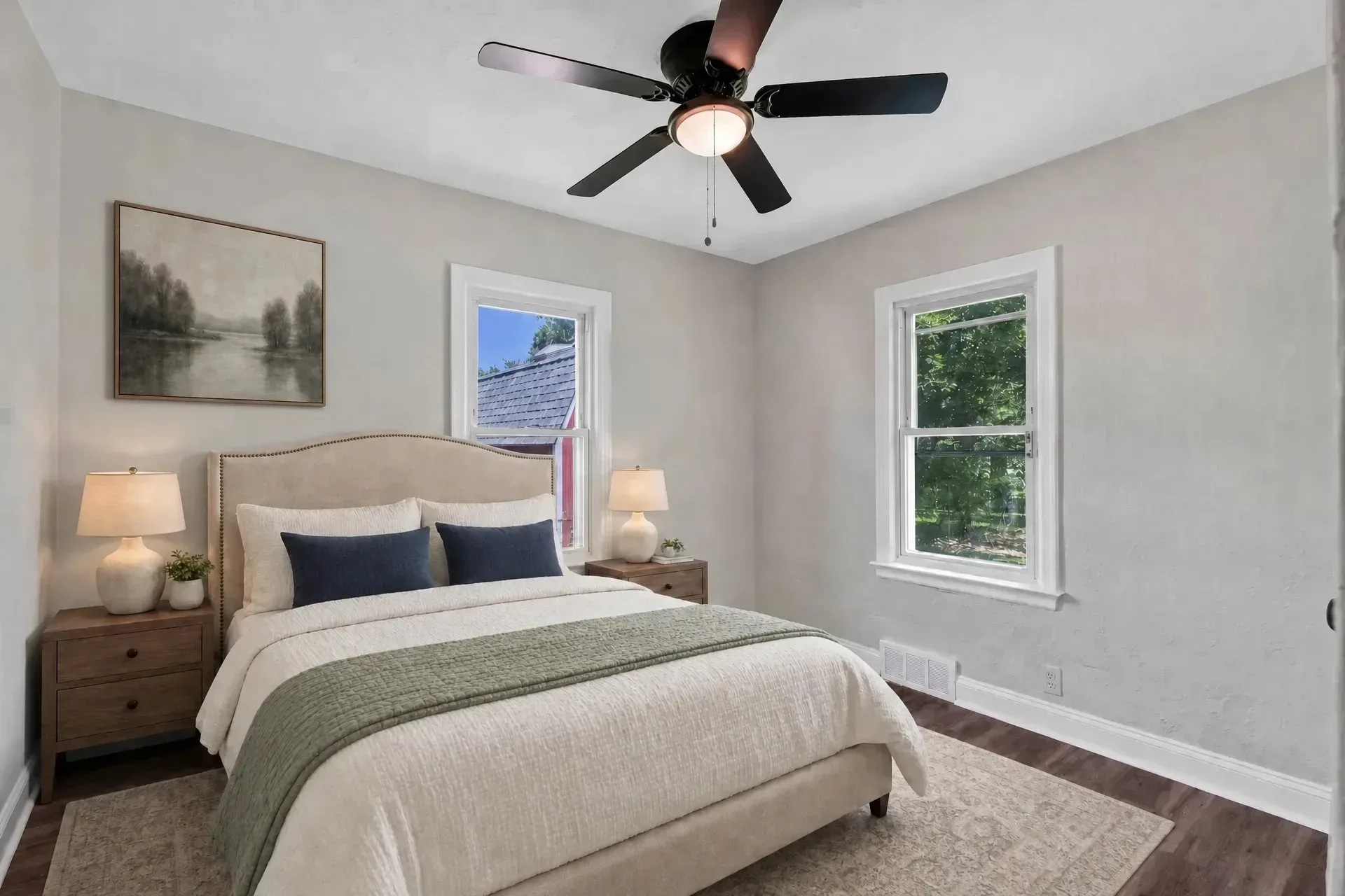 Second bedroom staged with upholstered headboard, bedding, nightstands, lamps, area rug, and wall art