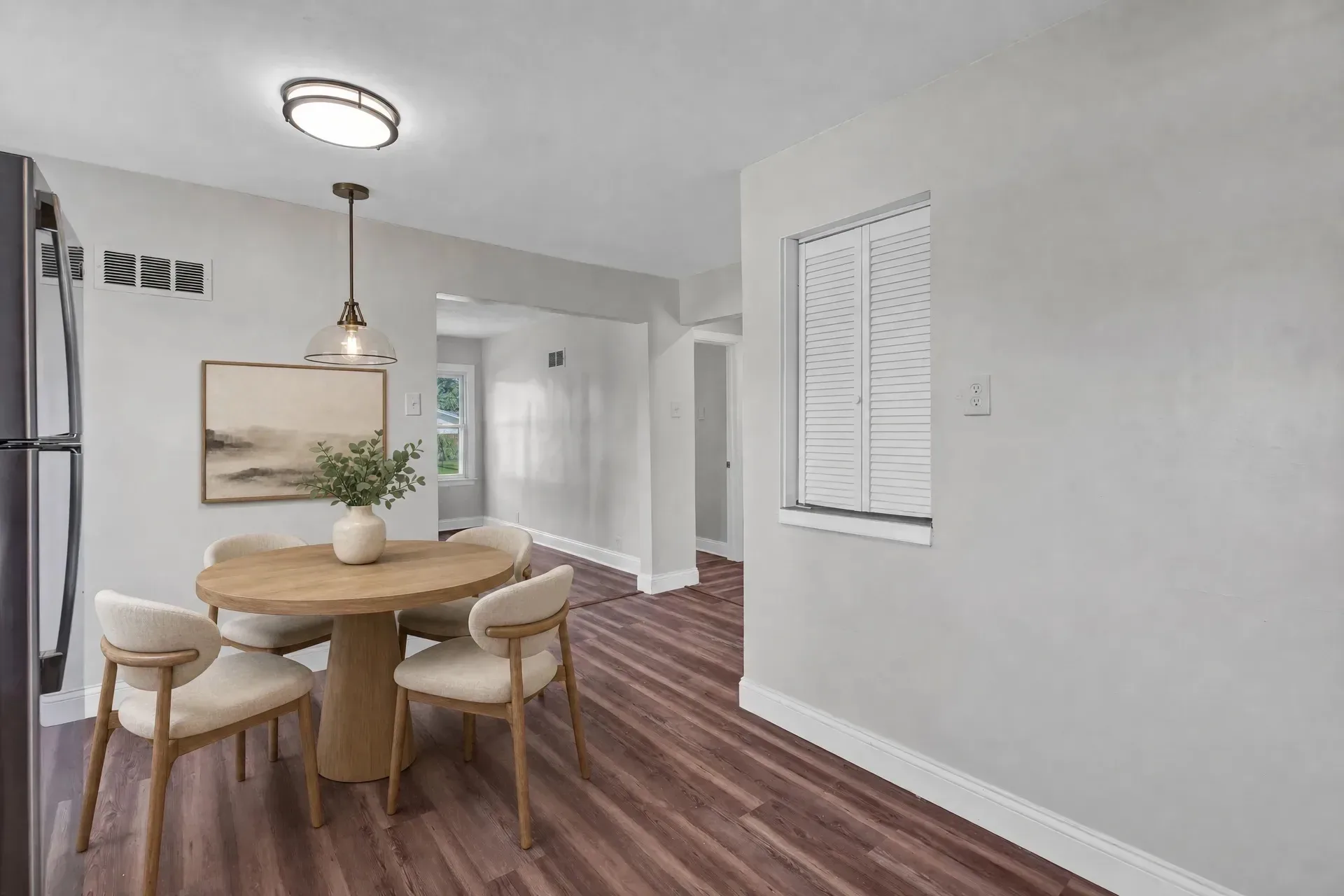 Breakfast room staged with round wooden table, four chairs, floral centerpiece, and wall art adjacent to the kitchen