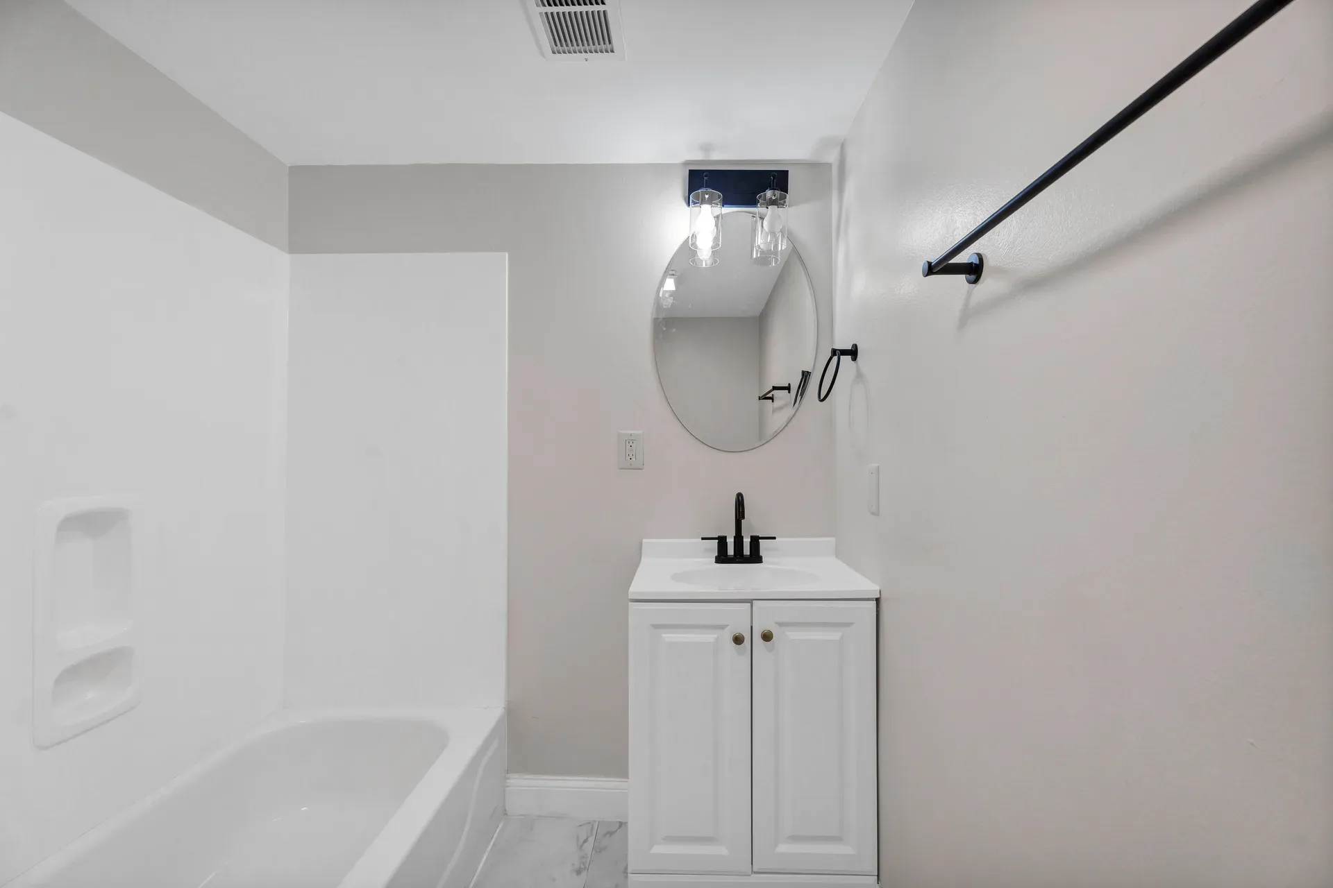 Lower level bathroom with white vanity, black faucet, surround tub, oval mirror, and overhead light fixture