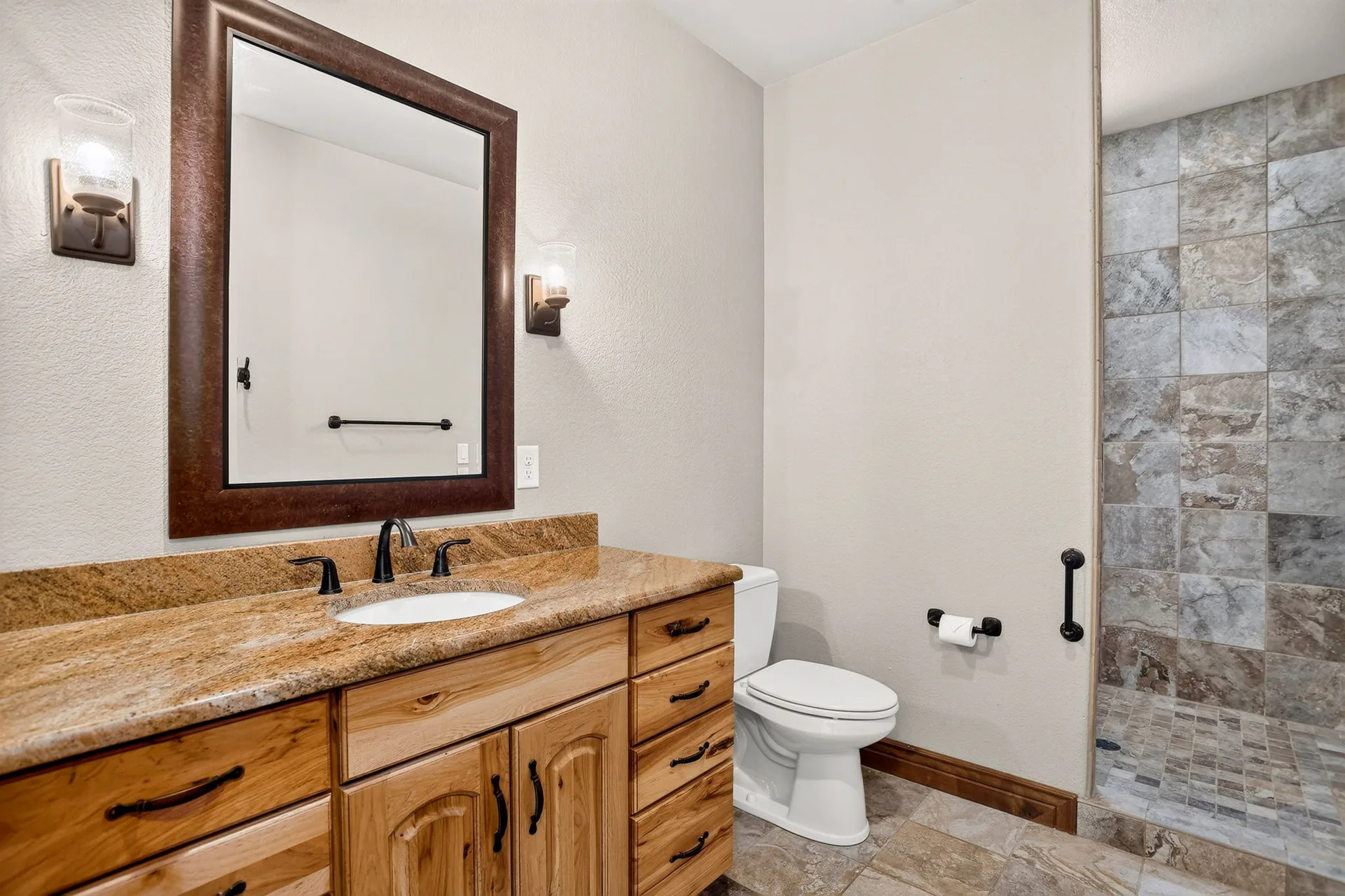 Bathroom with wood vanity, granite counter, and tile shower