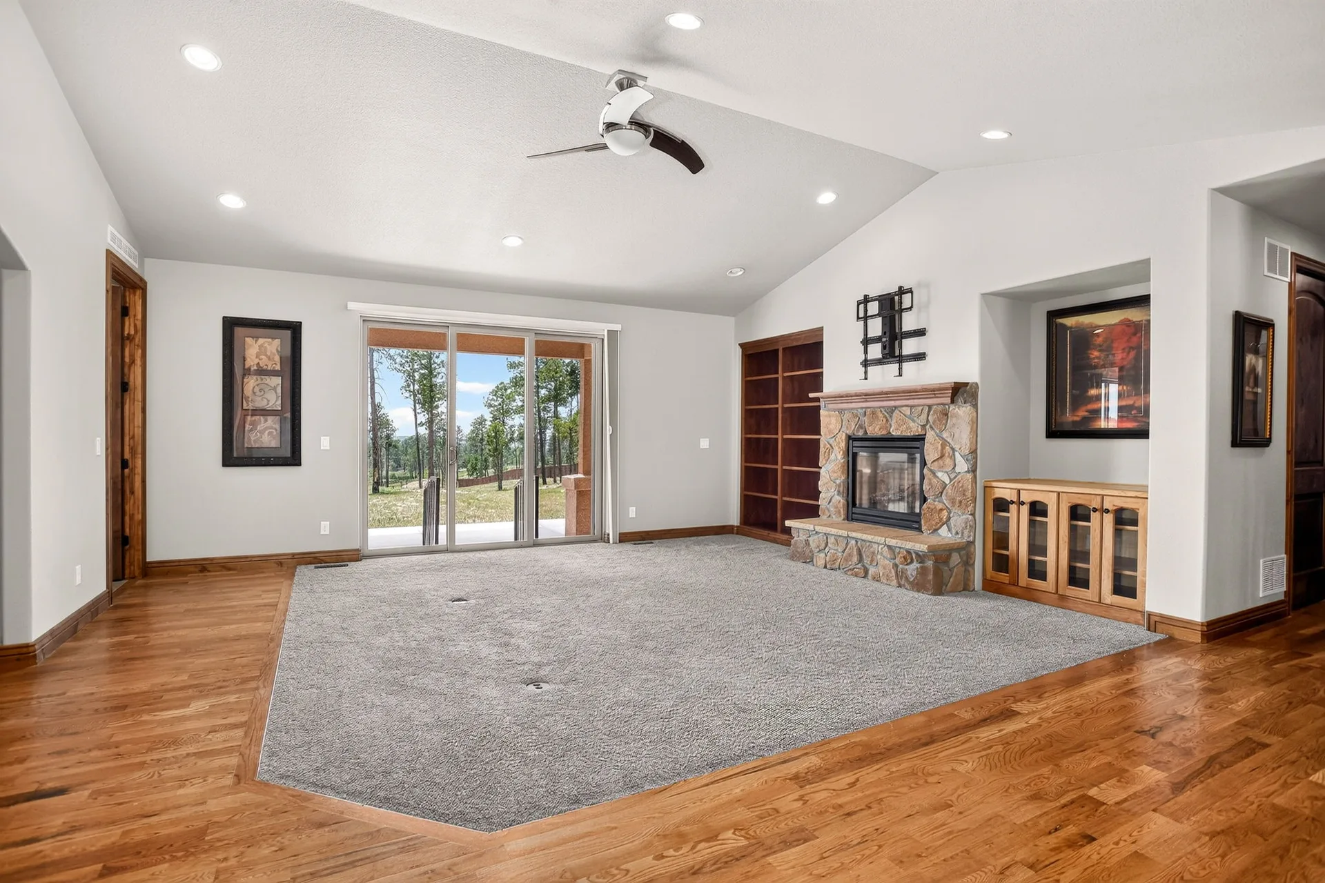 Living room with stone fireplace, built-in shelving, and vaulted ceiling
