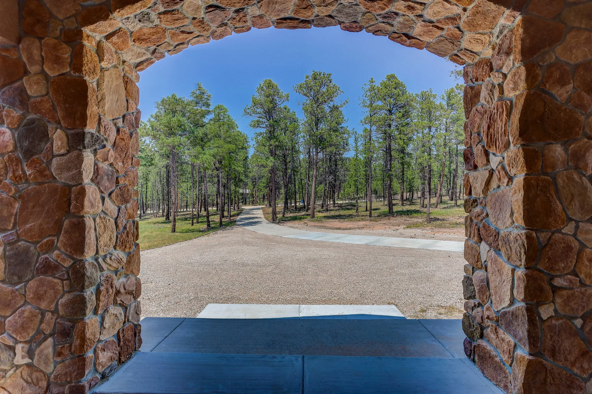 Stone archway entry framed by Ponderosa pines at 6905 Wildridge Rd.