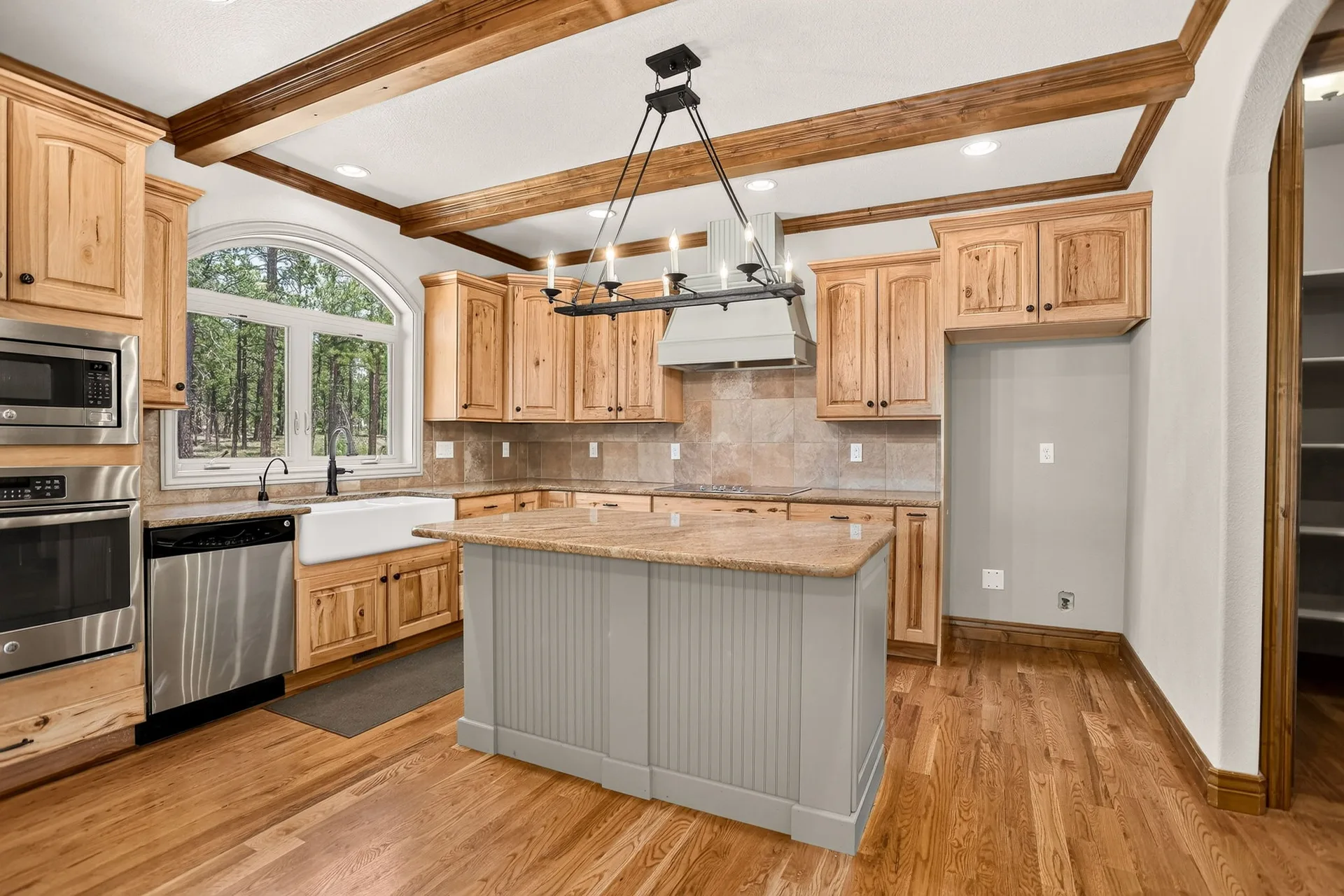 Rustic farmhouse kitchen with knotty alder cabinets, granite countertops, exposed ceiling beams, and a painted gray island