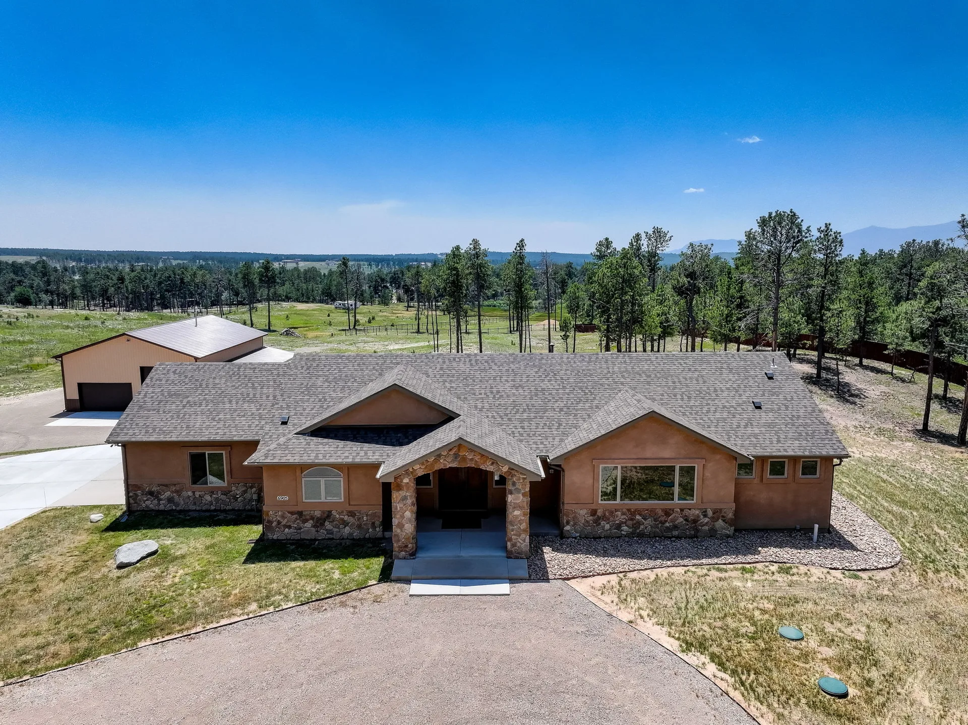 Aerial view of the ranch home with stone veneer accents among pine trees