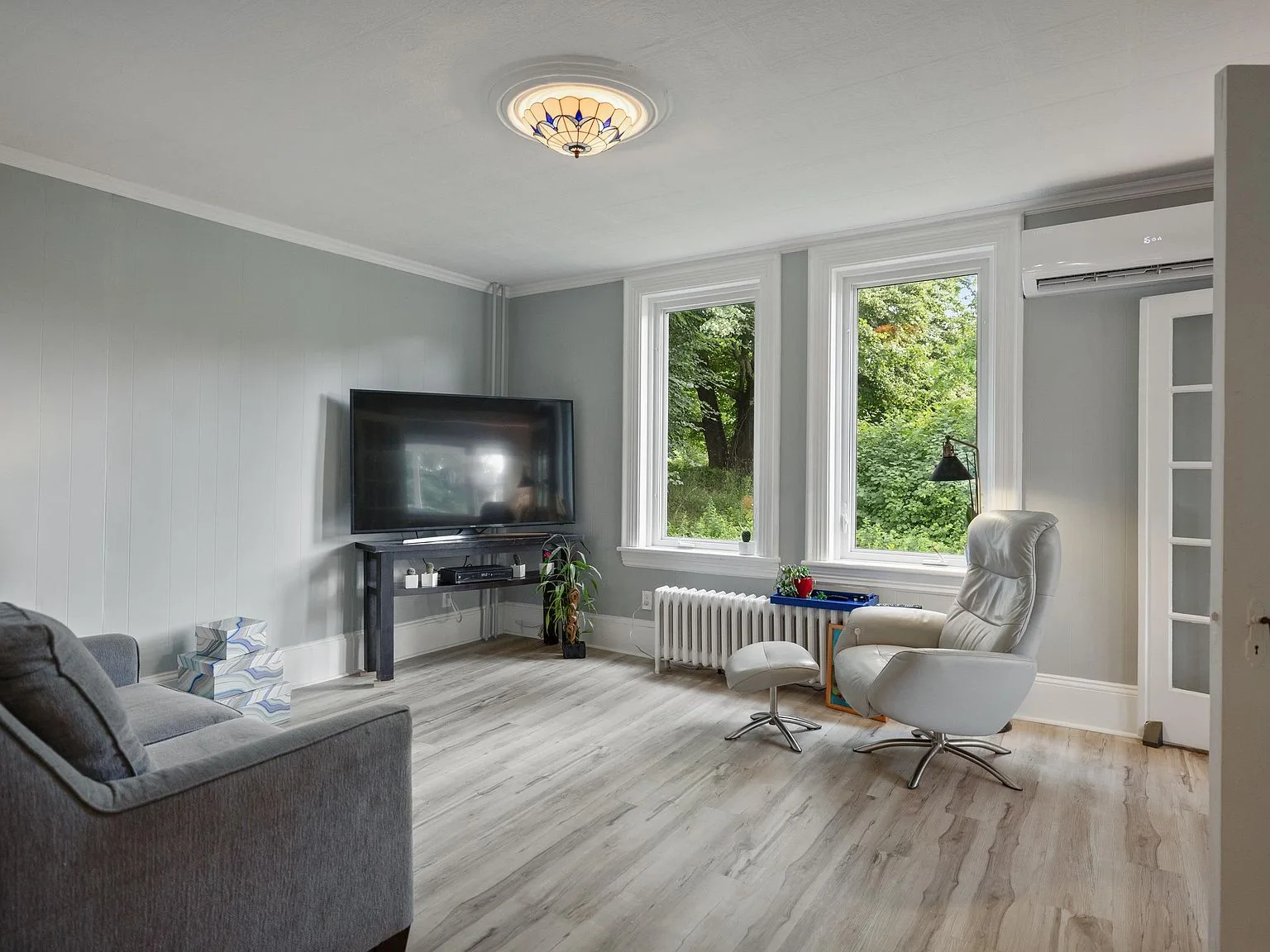 Living room with hardwood-style flooring and windows overlooking greenery