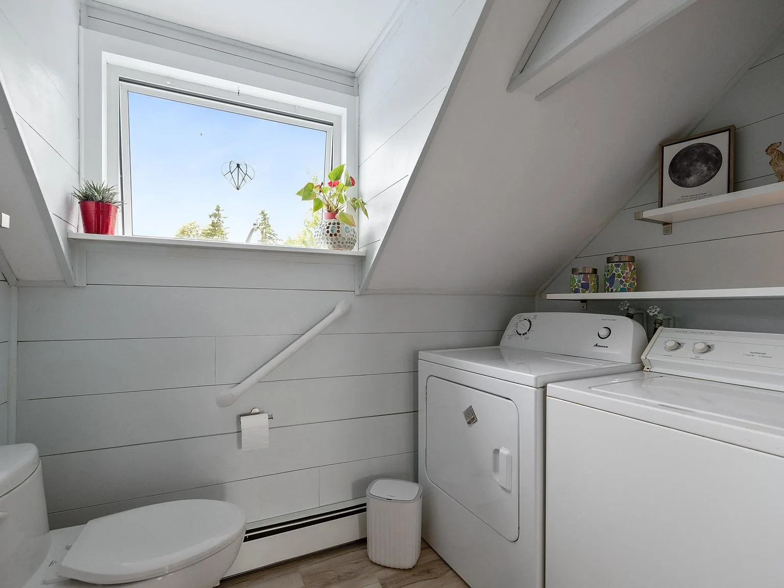 Laundry and bathroom space with white shiplap walls and angled ceiling