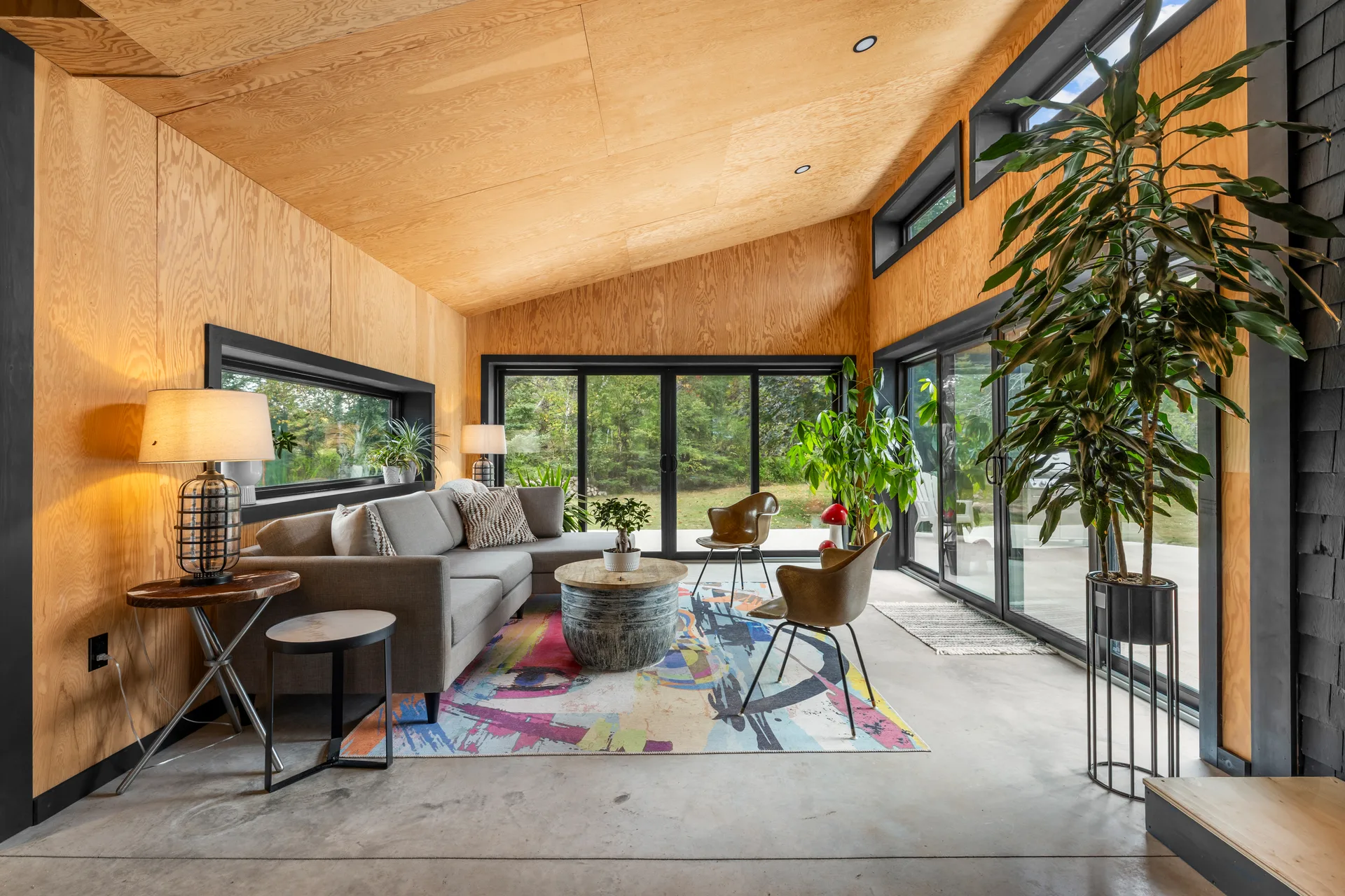 Light-filled sunroom with plywood paneling, concrete flooring, and floor-to-ceiling glass sliding doors
