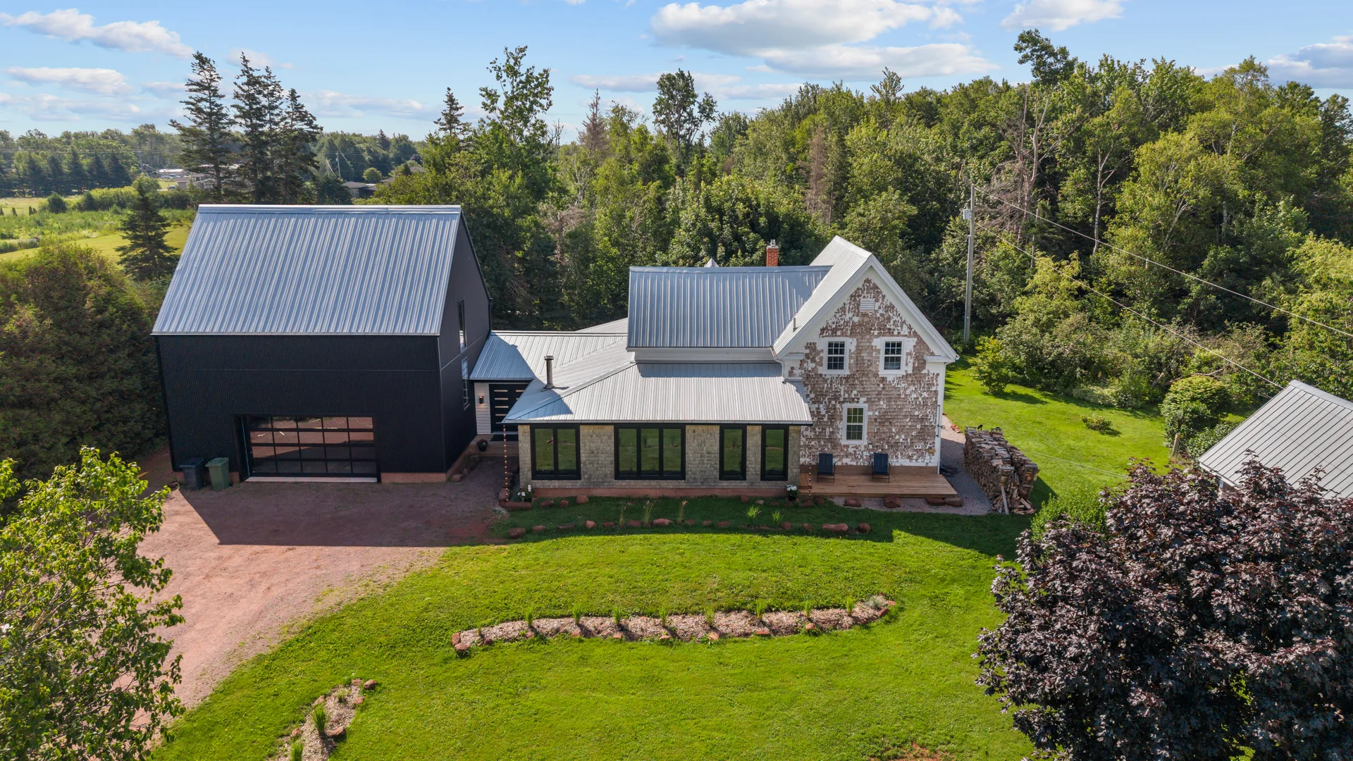 Aerial view of the restored 1870s farmhouse with modern barn-inspired addition, metal roof, and stone-and-stucco siding