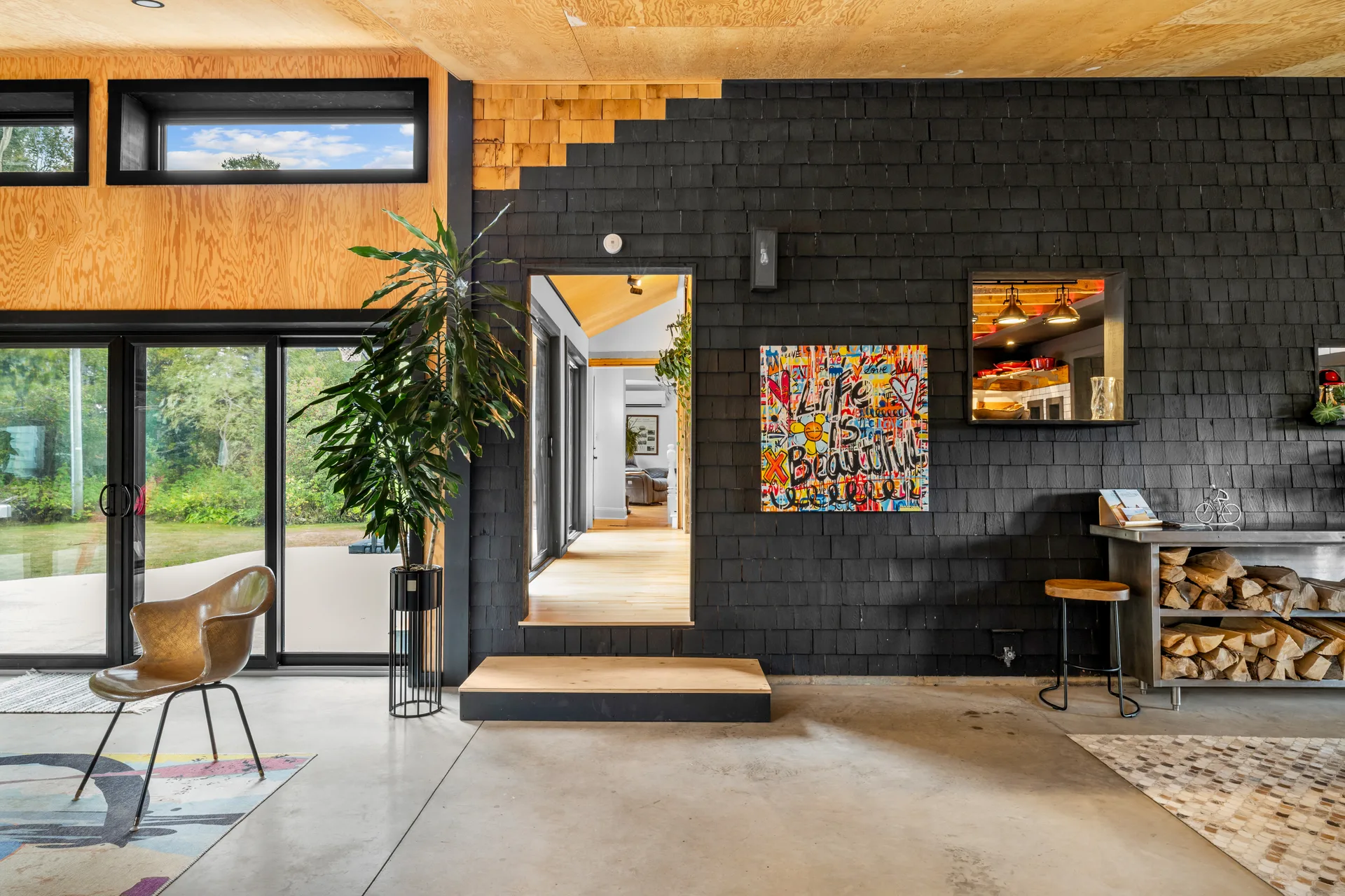 Living room with high-contrast black shingle-style wall, natural plywood ceiling, and concrete flooring