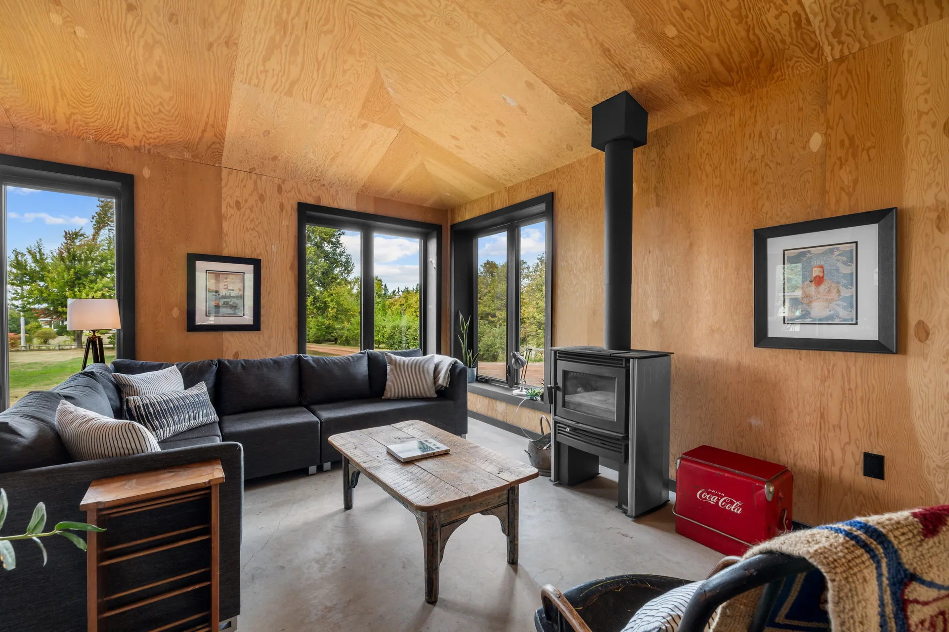Living room with natural plywood paneling, contemporary wood stove, and modern black window frames