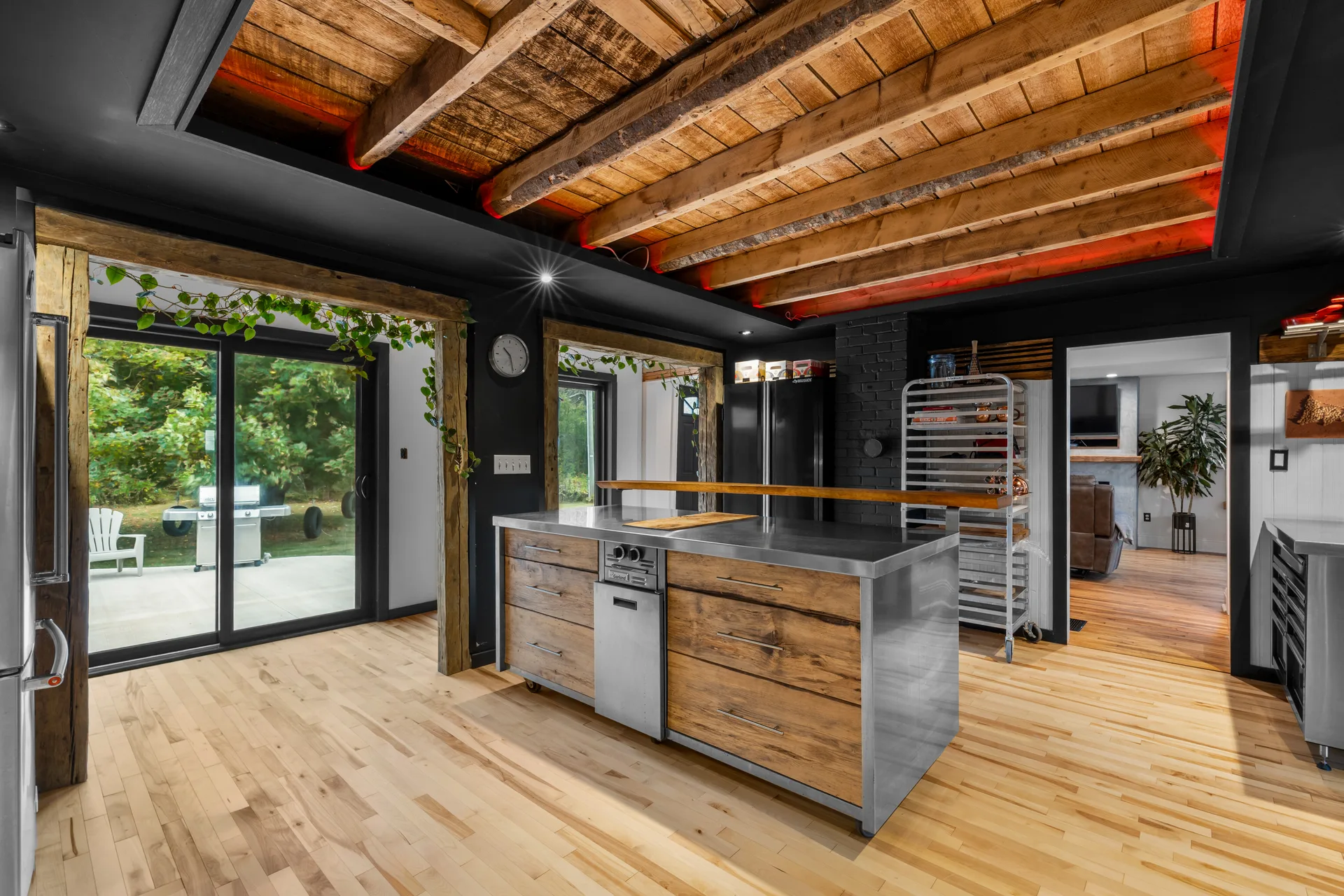 Wide-angle kitchen view with stainless steel island, wood-beam ceiling, and light hardwood floors