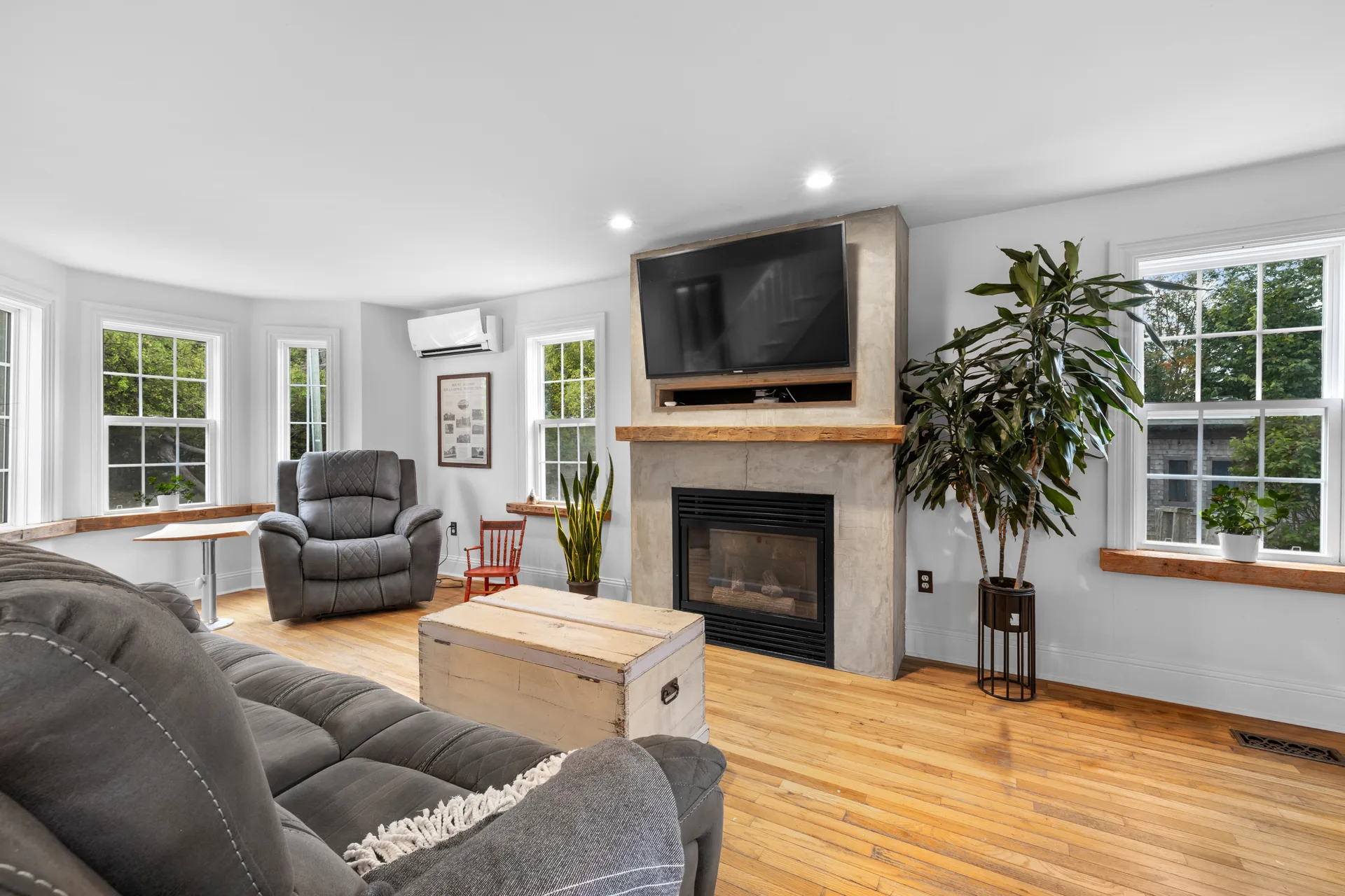 Farmhouse living room with hardwood floors, light walls, and stone fireplace mantle