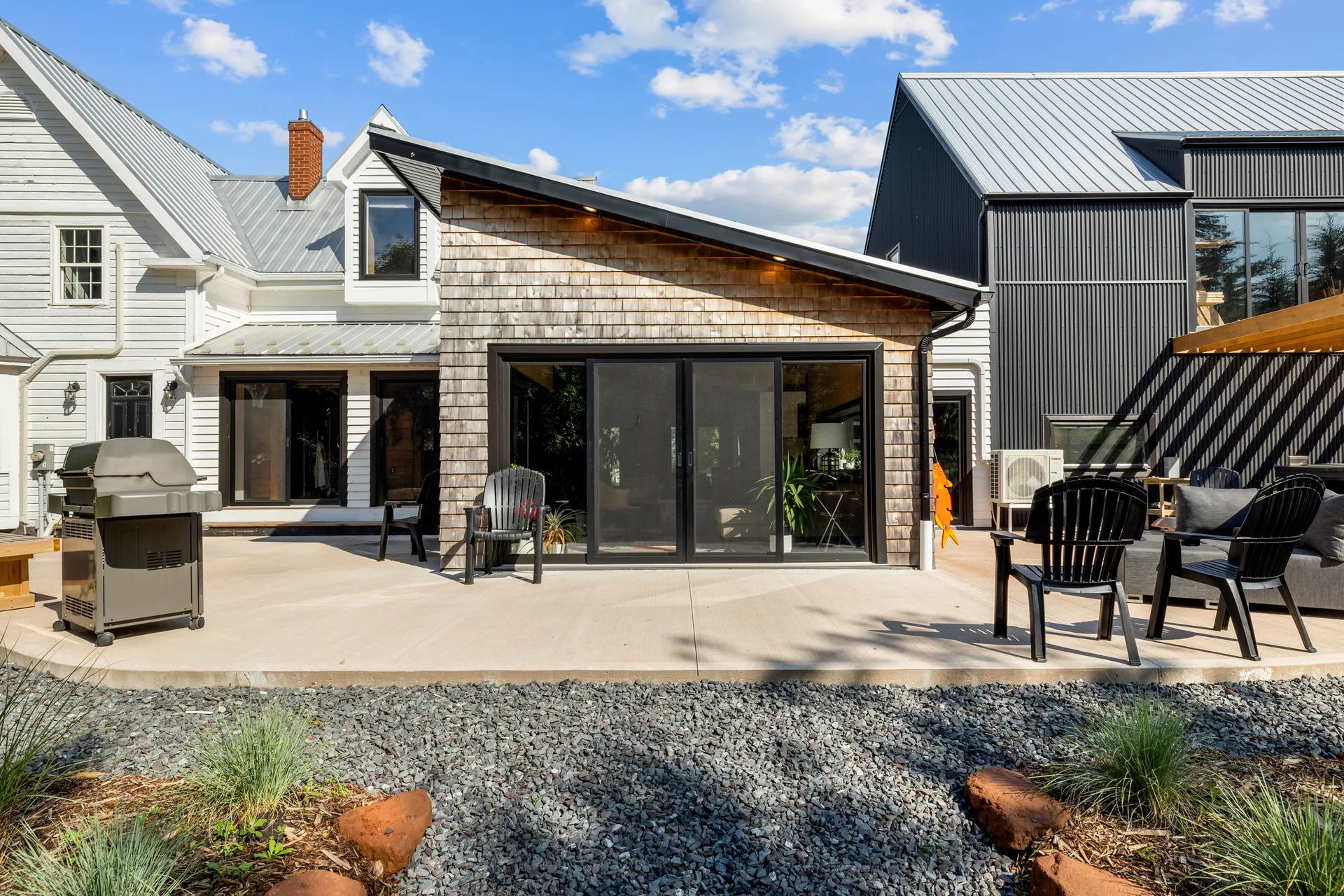 Backyard patio area showing the blend of classic white farmhouse, cedar shingle siding, and modern black metal siding
