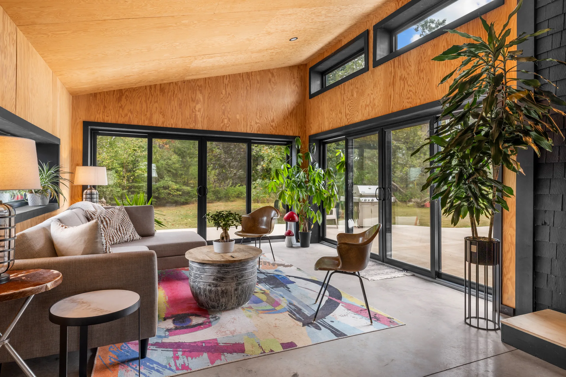 Wide-angle sunroom living area with light wood plywood walls, polished concrete flooring, and views to the patio