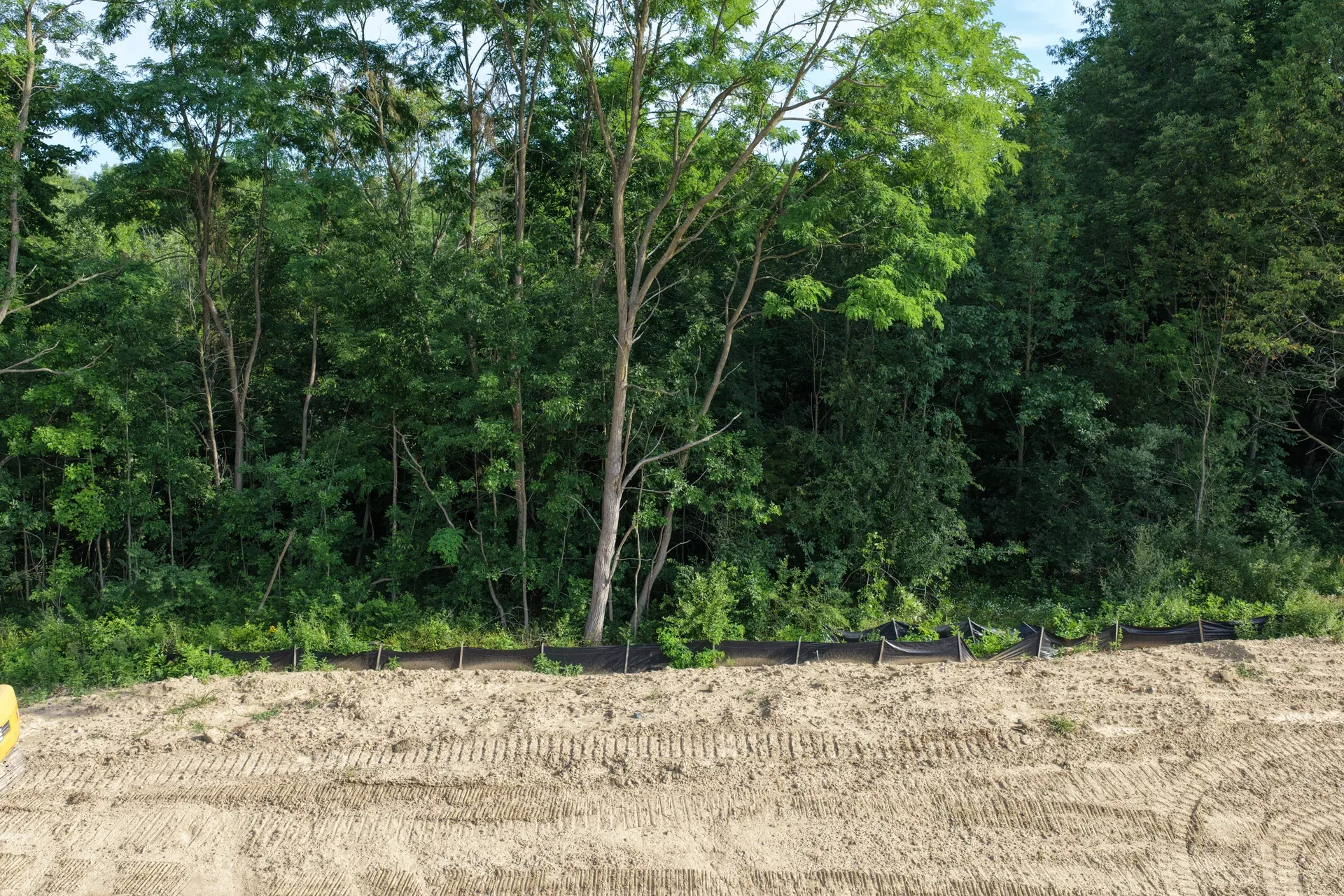 Drone aerial of a wooded construction lot at Oaks of Tyrone showing cleared building pad surrounded by mature trees in Tyrone Township Michigan