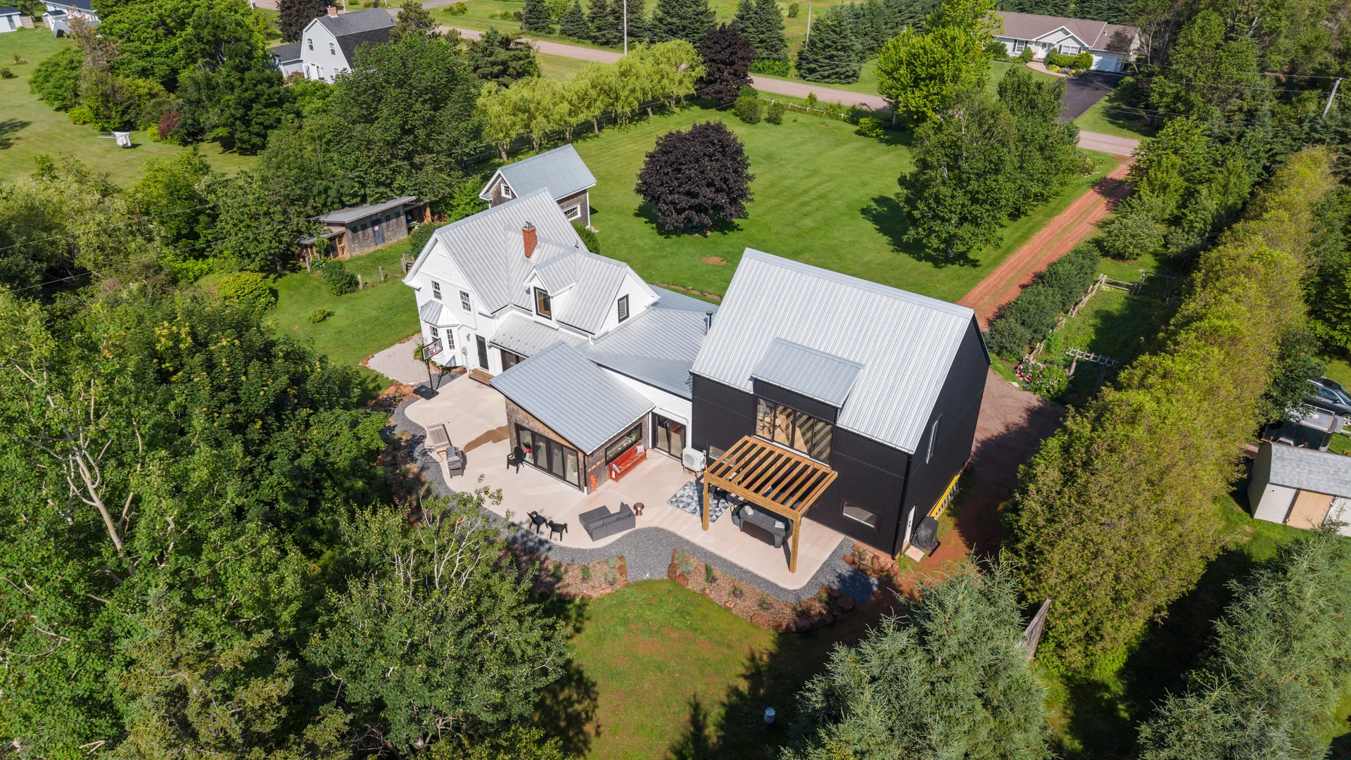 Drone aerial view looking down at the restored 1870s farmhouse with modern barn-style addition, patio, pergola, and lush grounds
