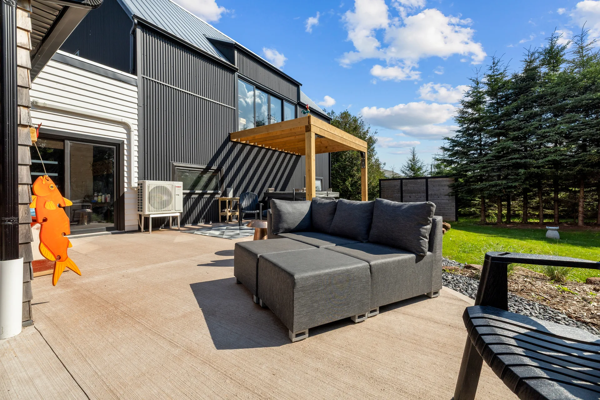 Backyard patio showcasing the modern barn-inspired addition with black metal siding, glass sliding doors, and wood pergola